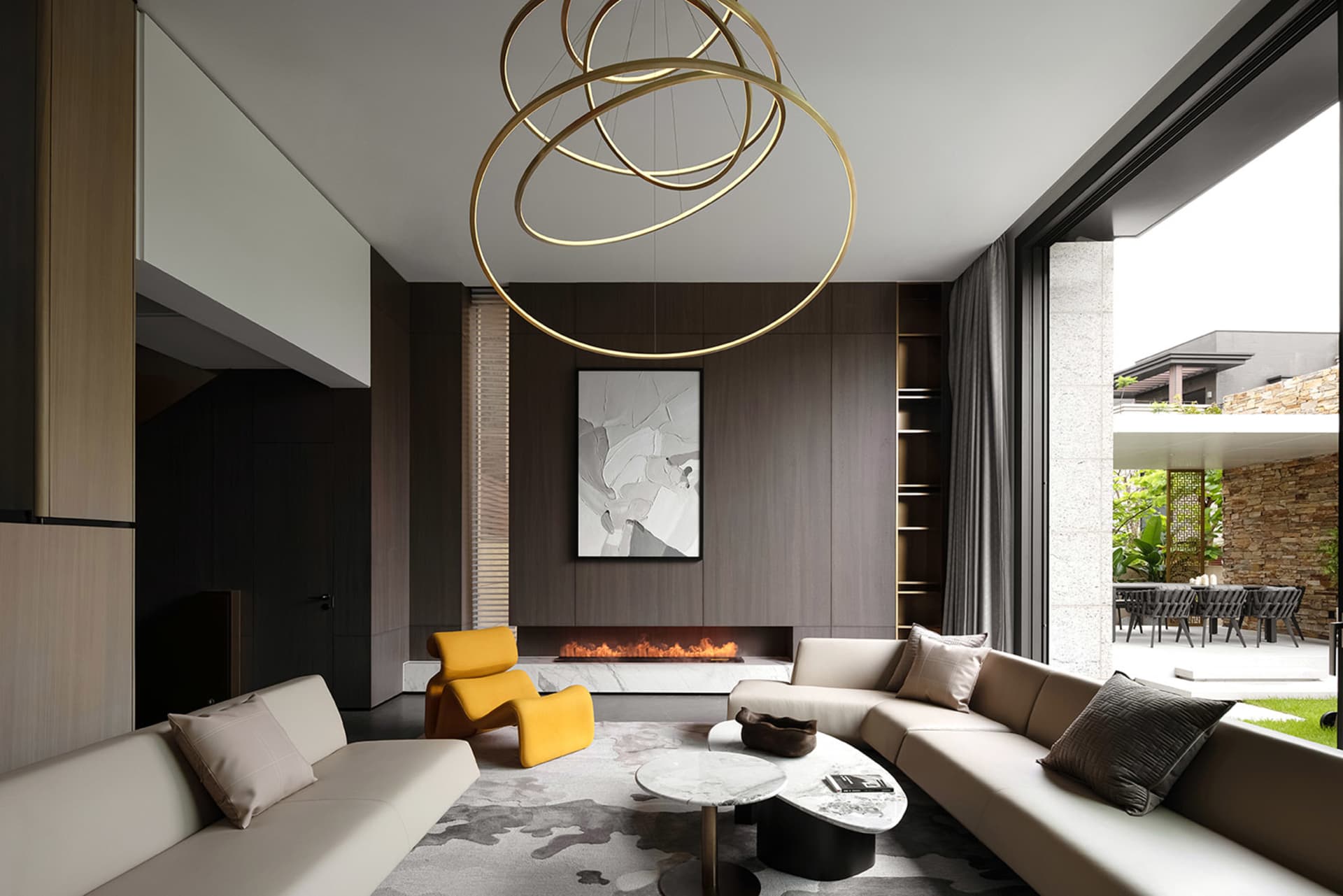 A modern living room with marble, glass, and wooden elements, featuring a fireplace, couches, and a contemporary chandelier.