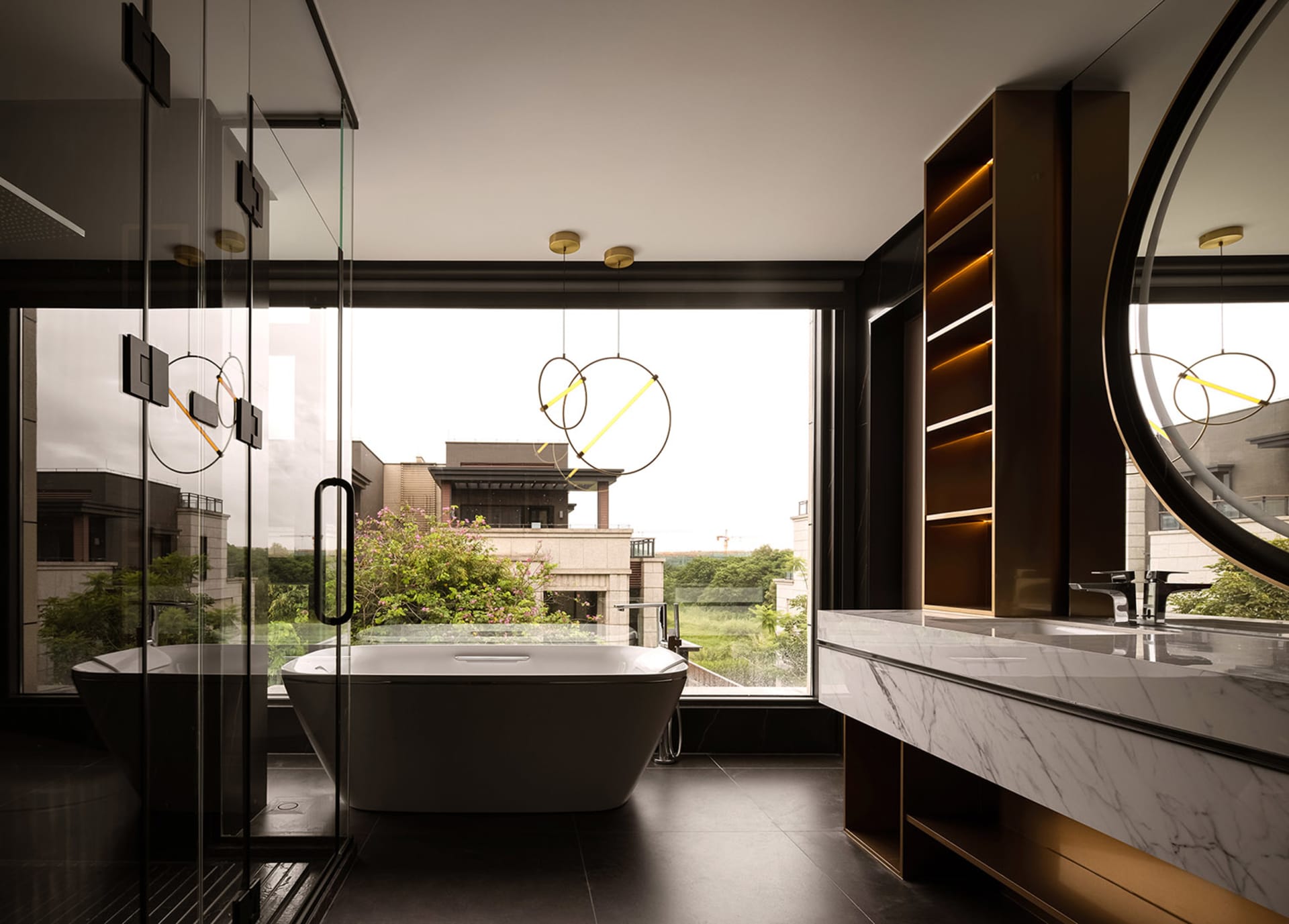 Modern bathroom with marble tub, glass shower, and large windows overlooking greenery.