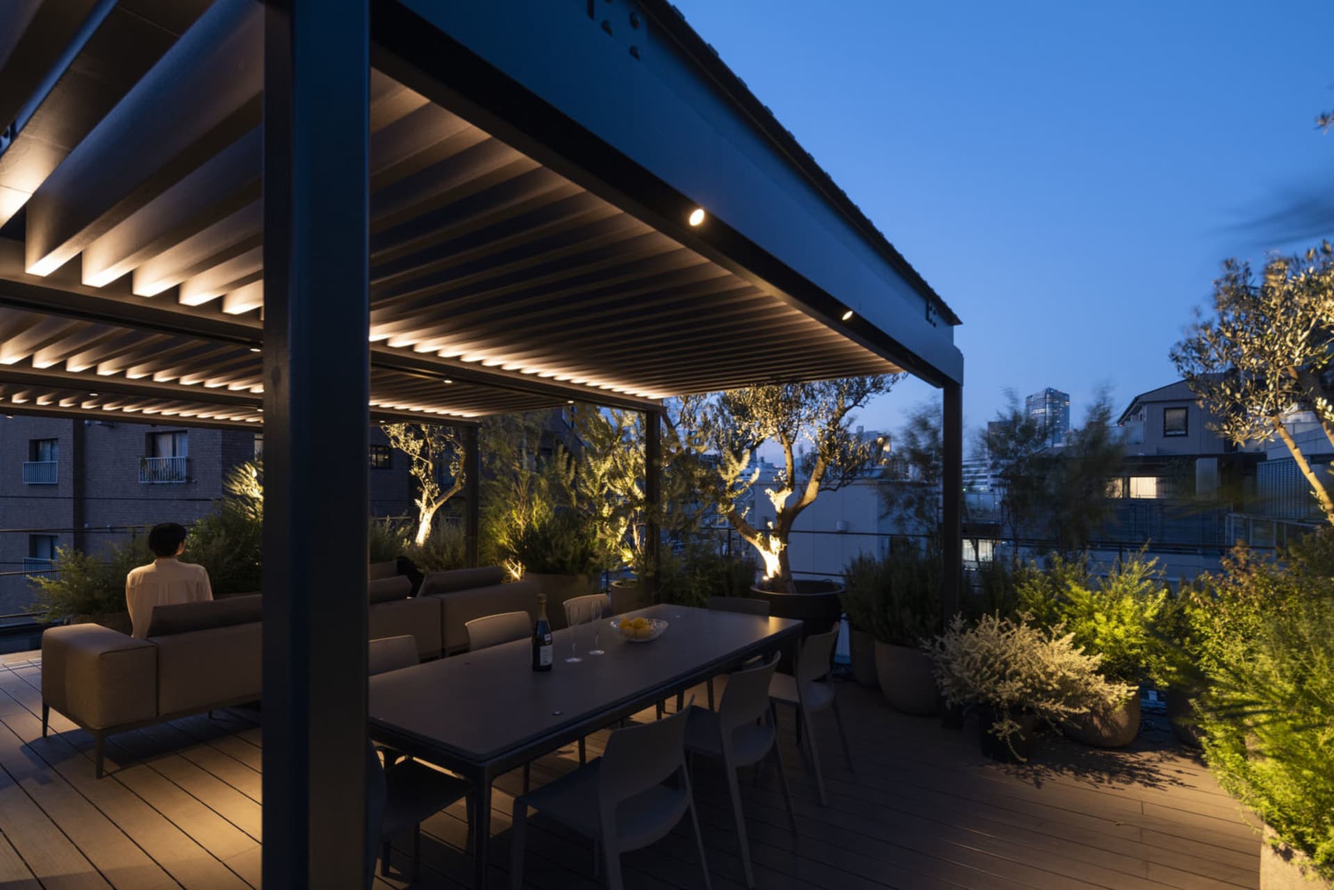 A modern, minimalist rooftop patio with concrete flooring, metal furniture, and LED lighting features.