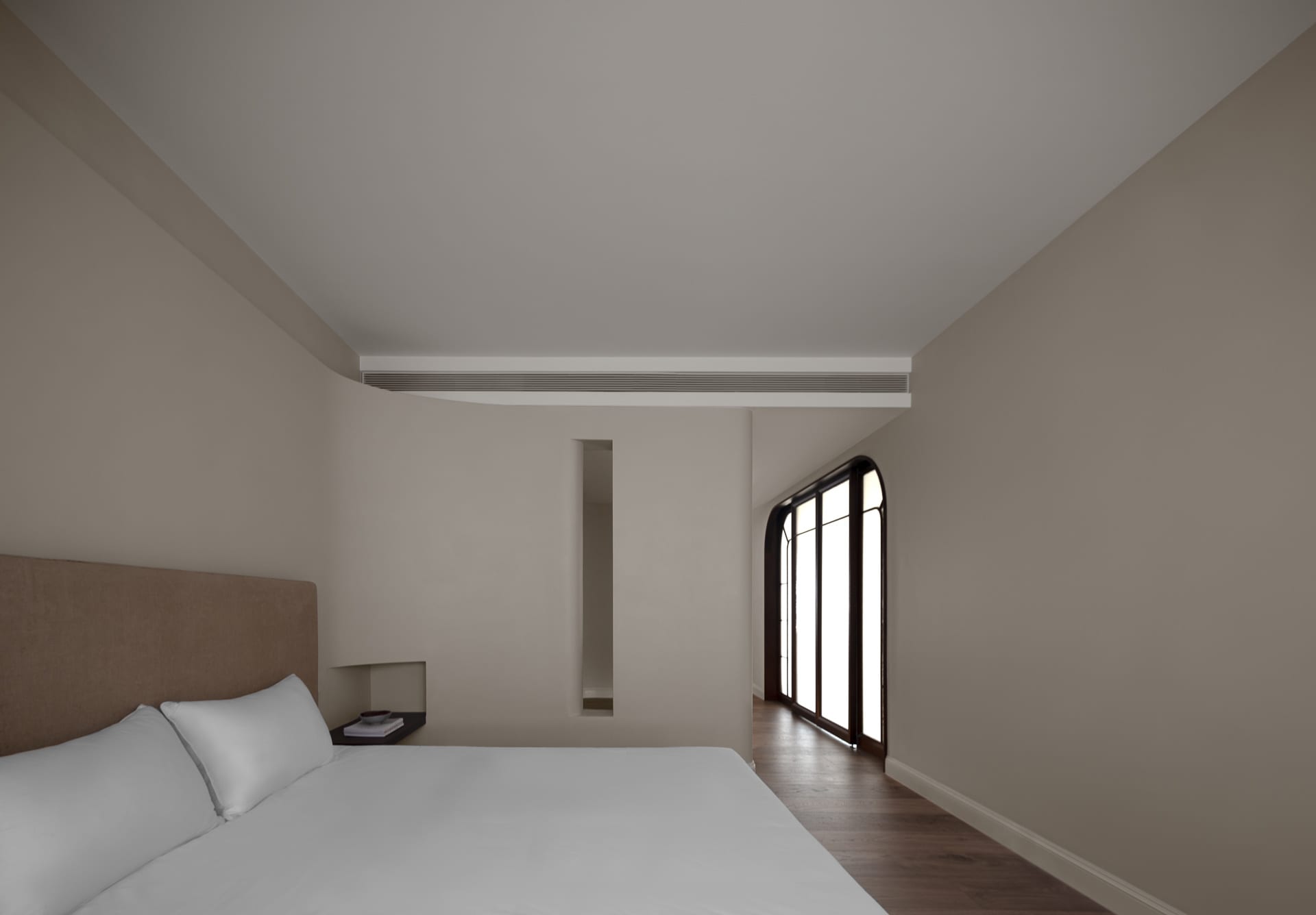 A minimalist bedroom with a white bed, wooden floor, and glass window.