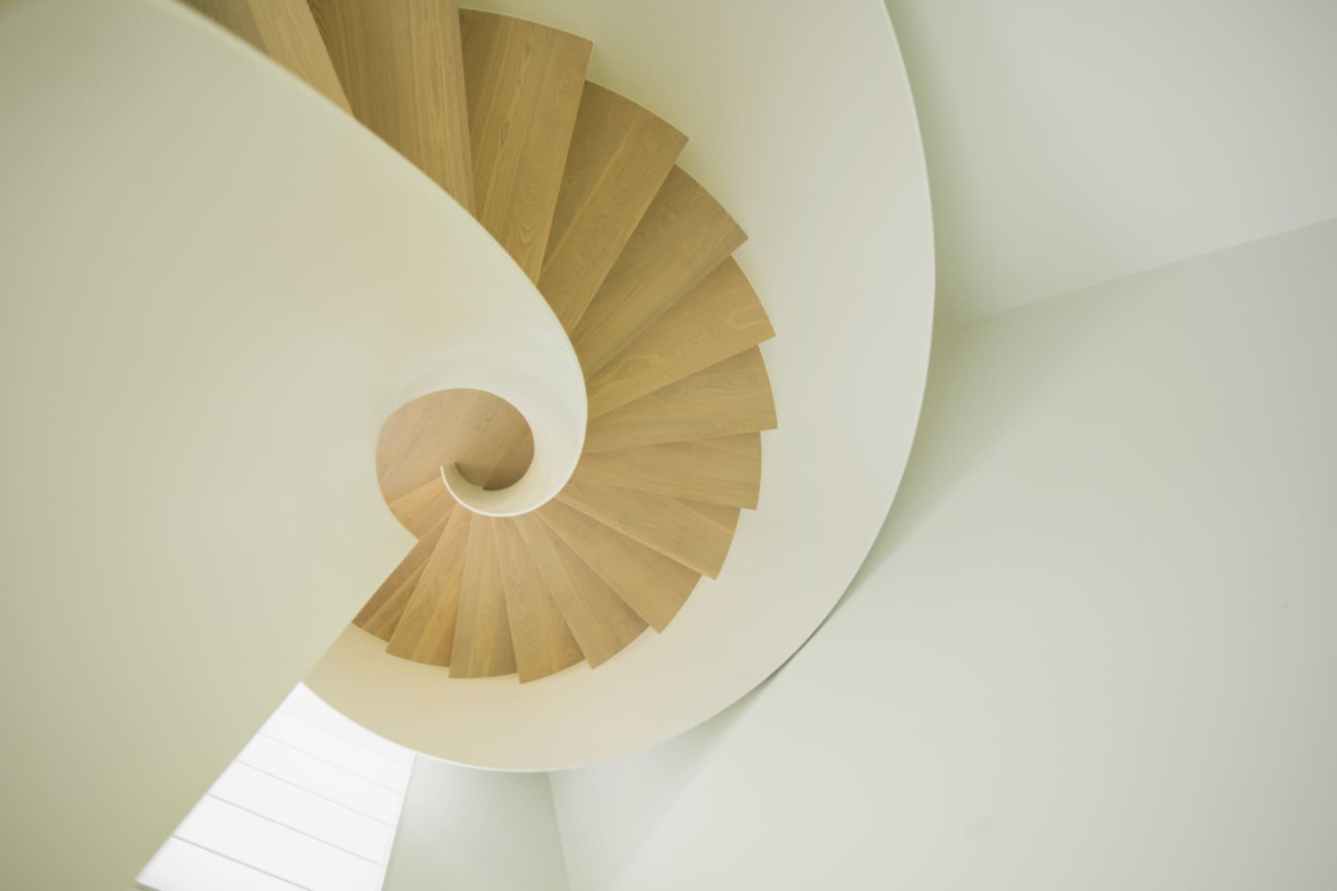 A modern, wooden spiral staircase with white walls