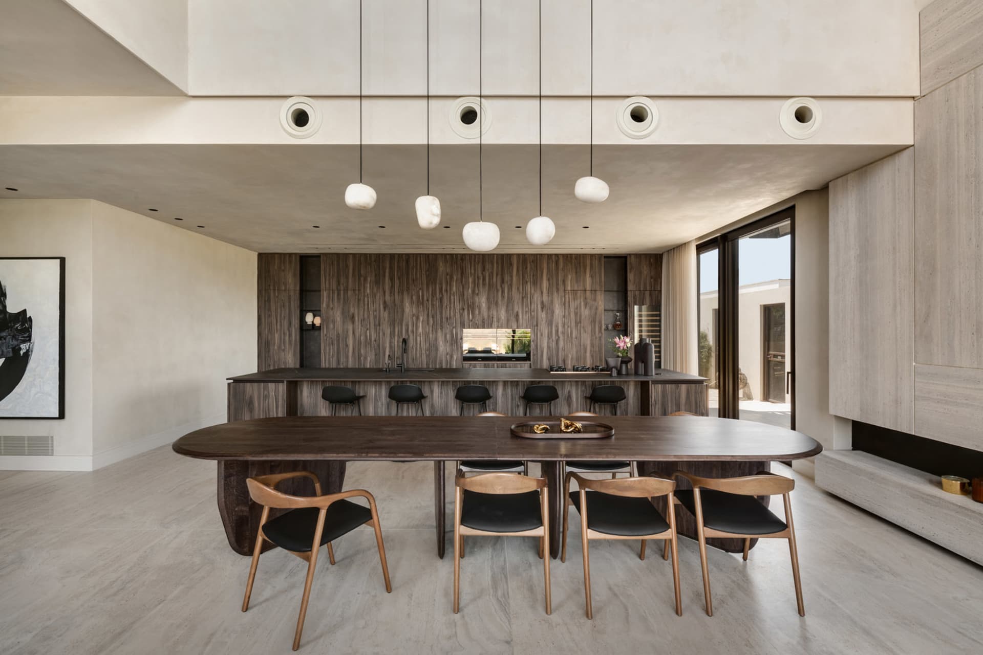 A modern dining room featuring a wooden table and chairs, set against a backdrop of a kitchen with wooden cabinets.