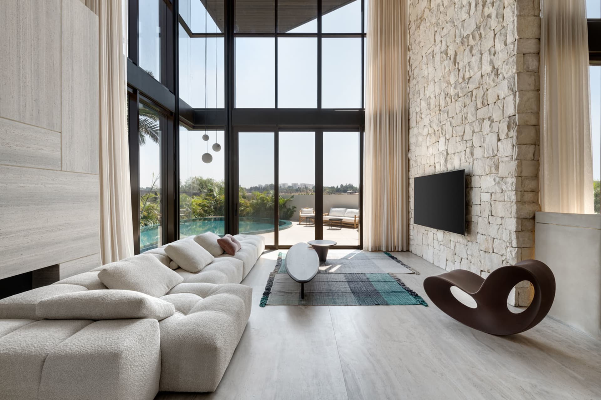 A spacious modern residential living room with a white tufted sofa, a minimalist coffee table, and a flat-screen TV mounted o