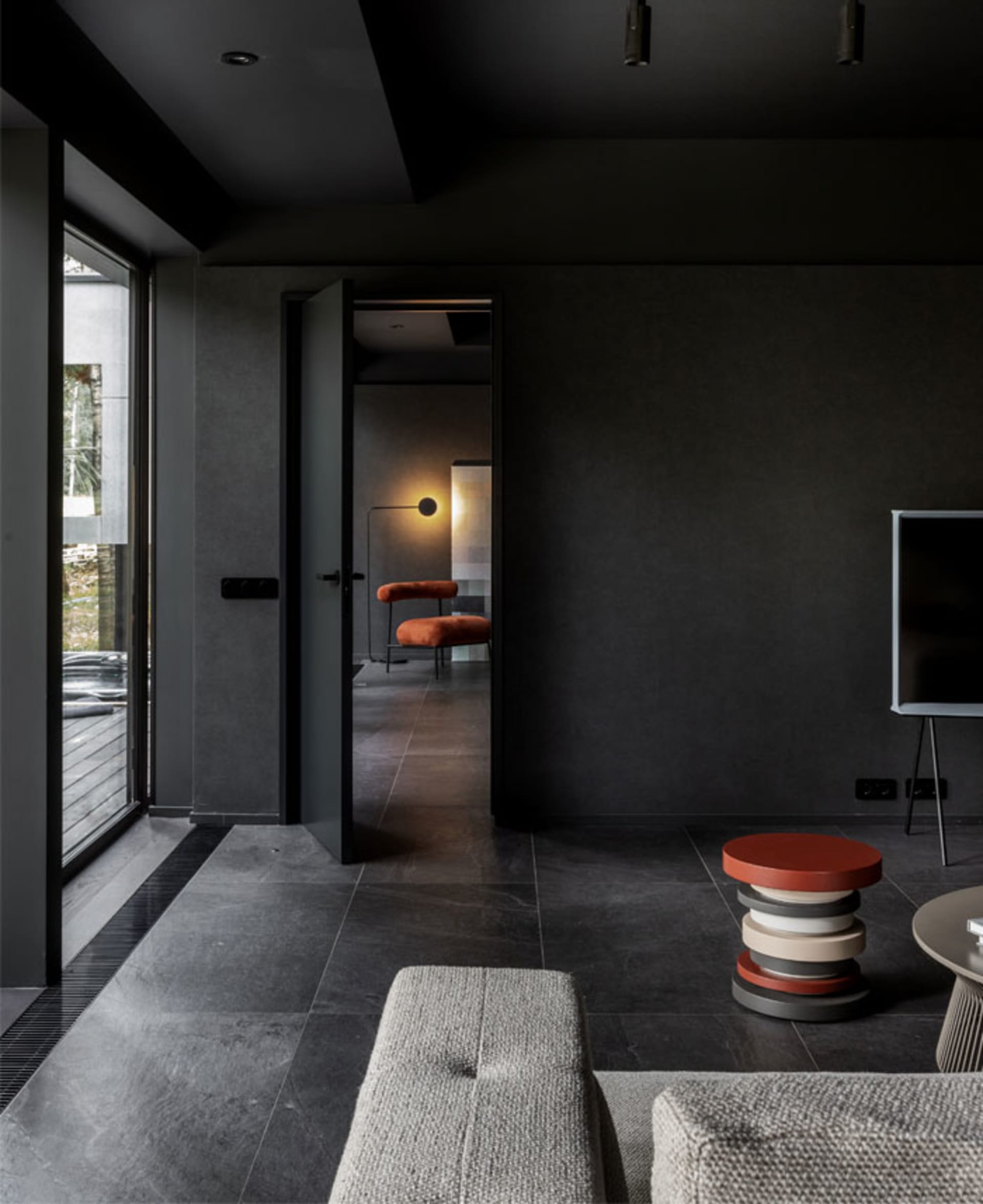 A modern living room with dark walls, concrete flooring, and metal furniture. A floor lamp is illuminating the space, and a t