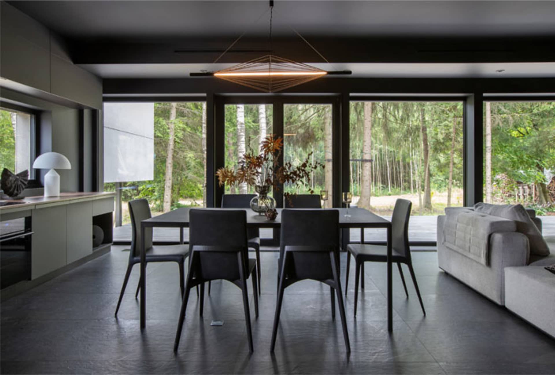 Modern minimalist dining room featuring black metal table and chairs with large windows showcasing natural forest view.