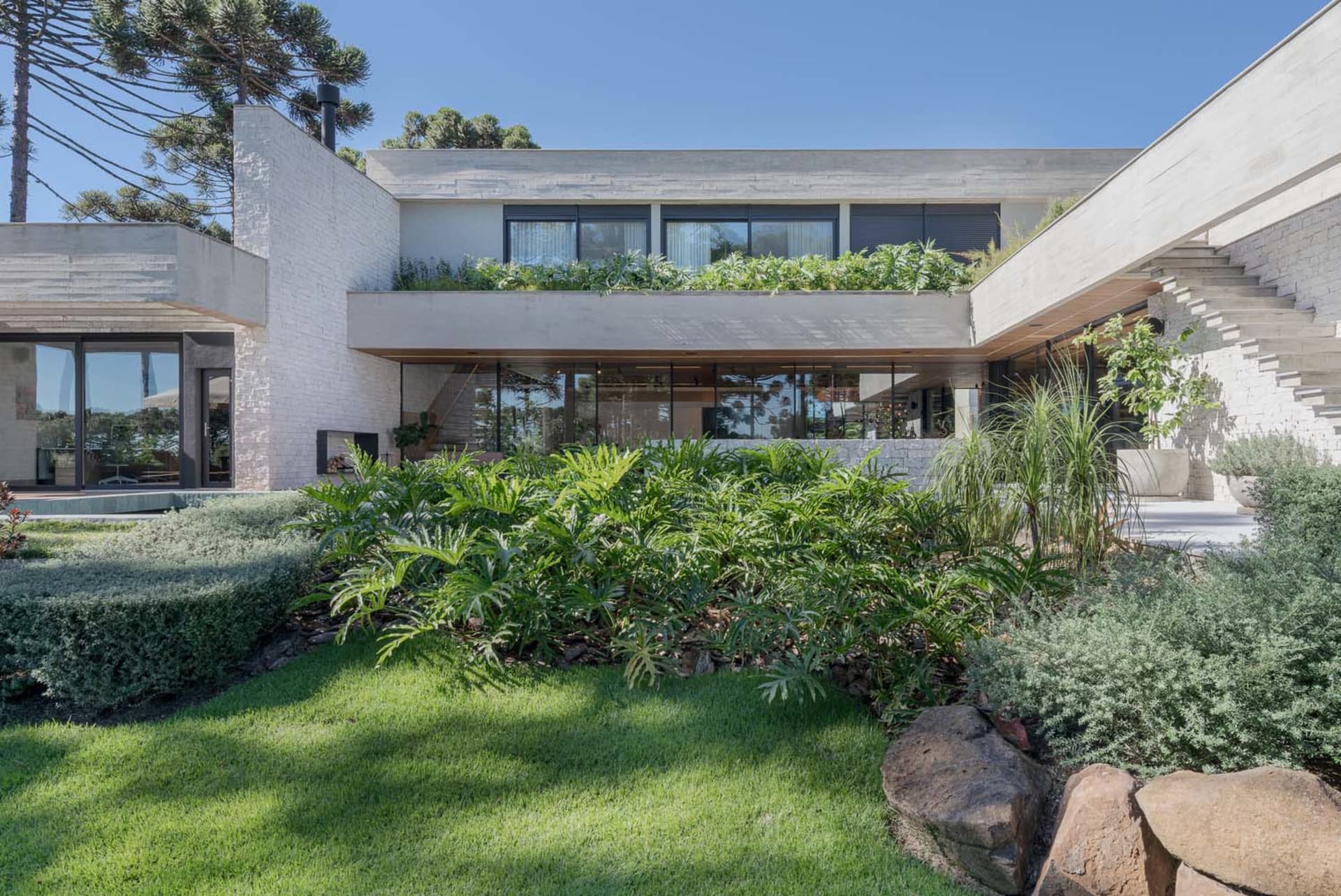 Modern residential exterior featuring a concrete structure with a rooftop garden and a well-maintained lawn.