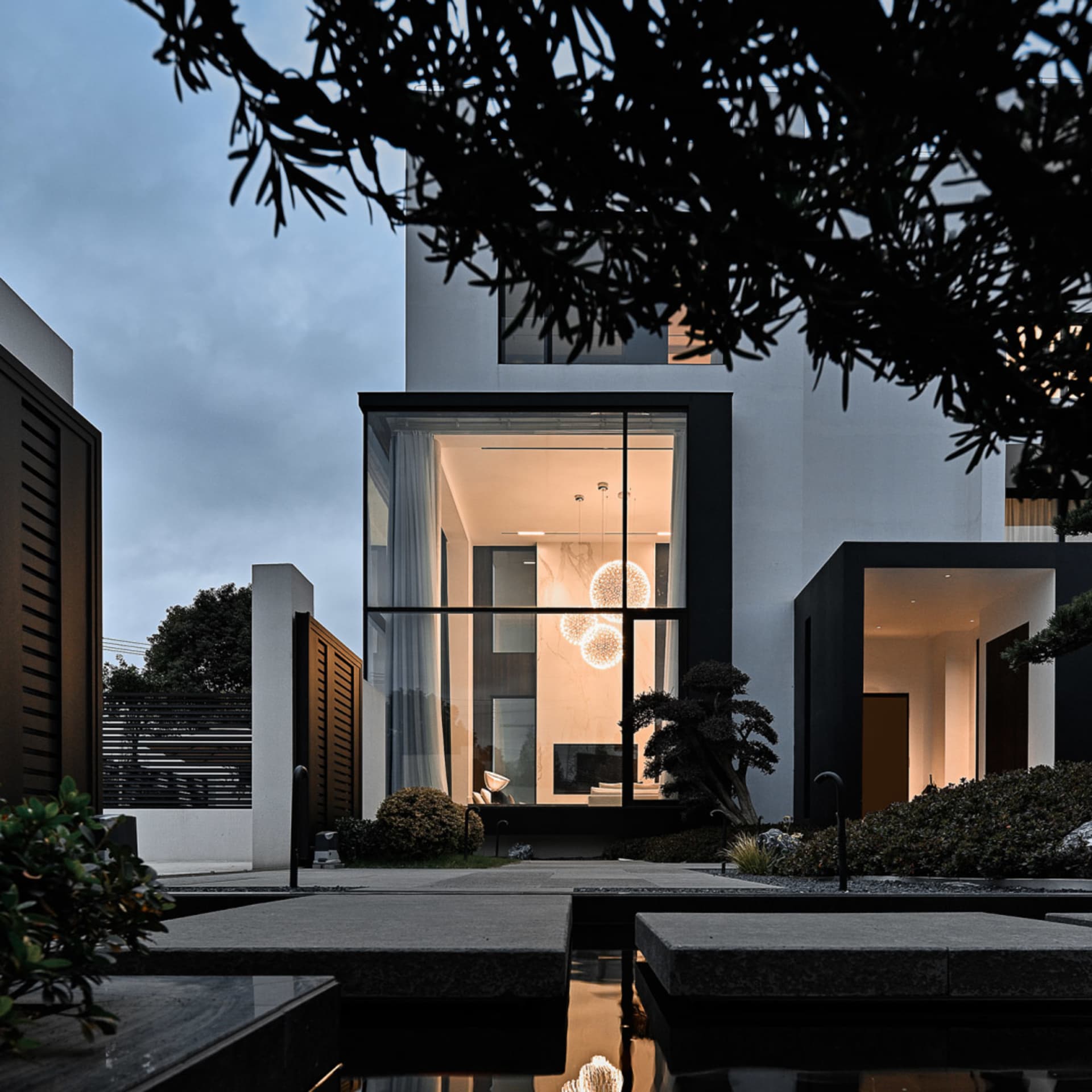 A modern residential home with a concrete exterior, illuminated by warm interior lights at dusk.