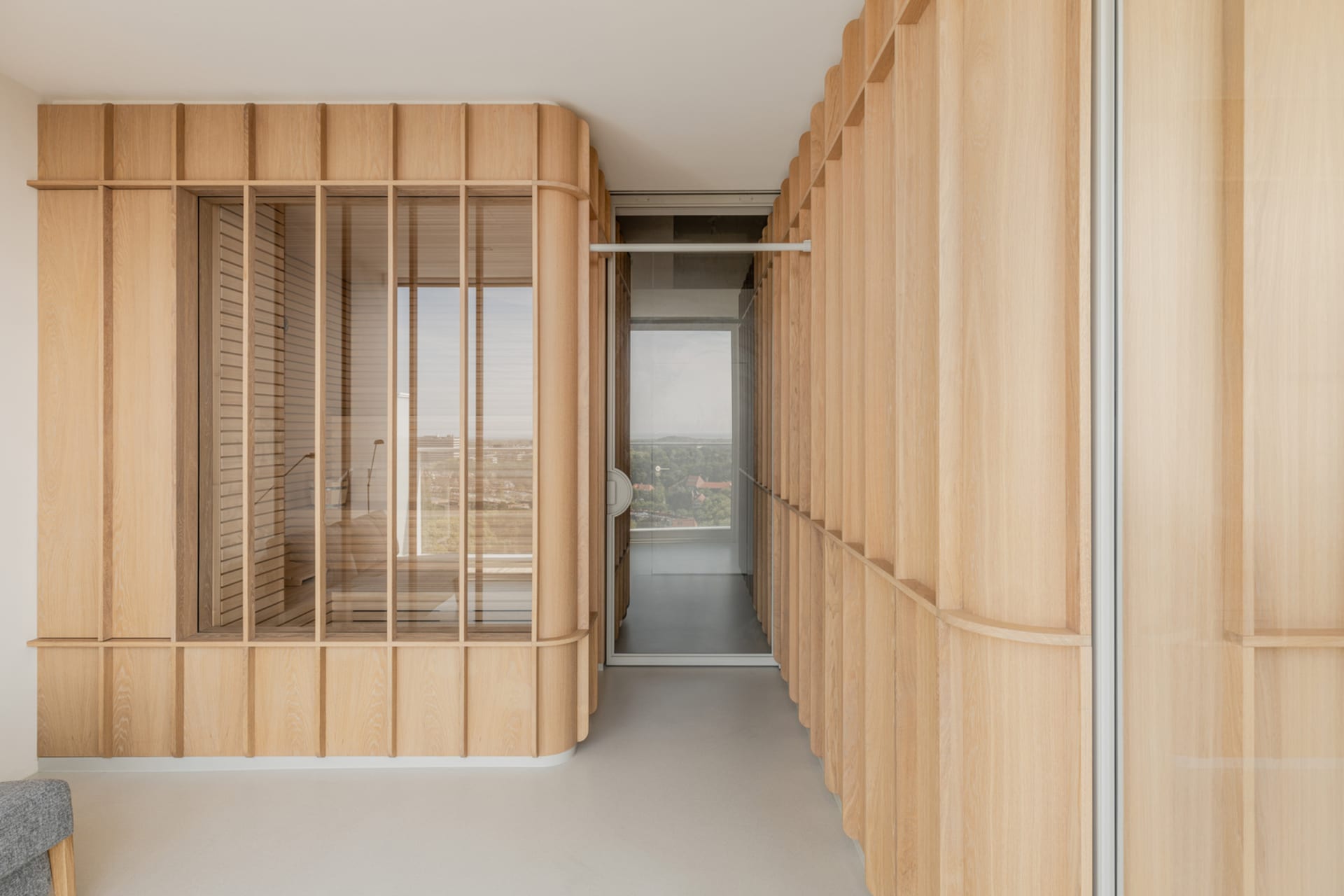 A spacious living room with wooden paneled walls, large windows, and a white floor.