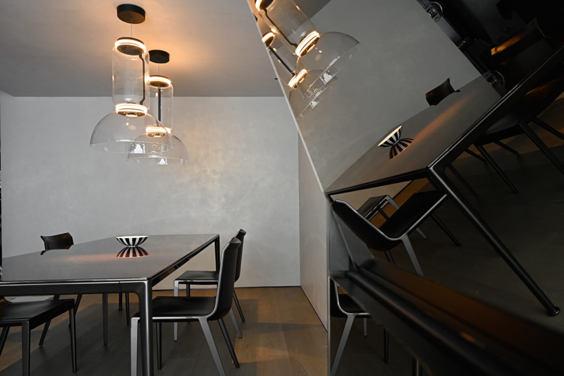 A modern minimalist restaurant interior with metallic tables and chairs, white walls, and clear pendant lights.