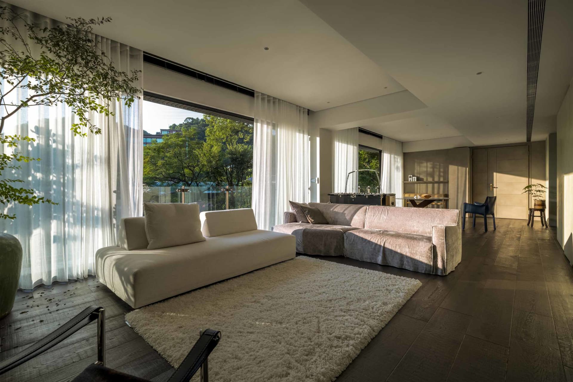 A modern living room featuring a white fabric sofa, a glass coffee table, and wooden flooring.