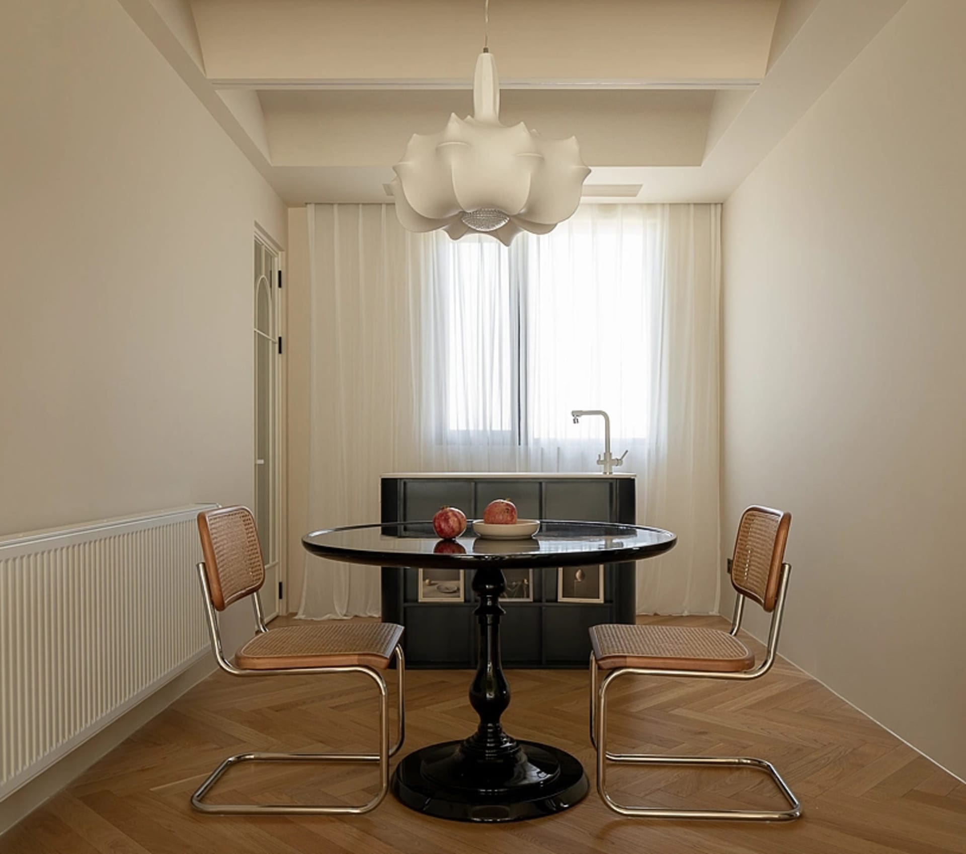 Modern minimalist dining room with black table and leather chairs, glass pendant light, and herringbone wood flooring.