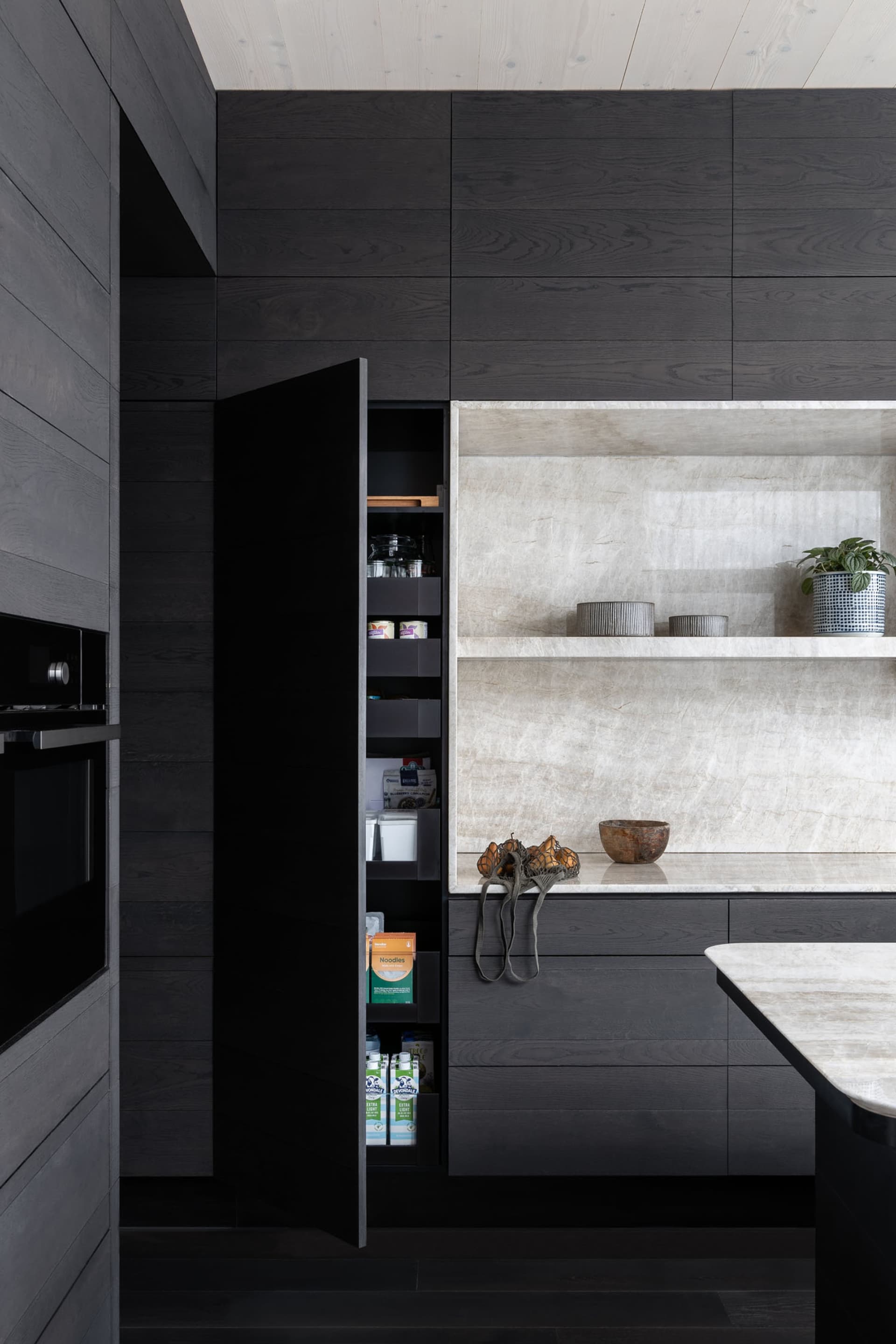 A modern minimalist kitchen featuring dark wood cabinets, marble countertops, and open shelving storage.