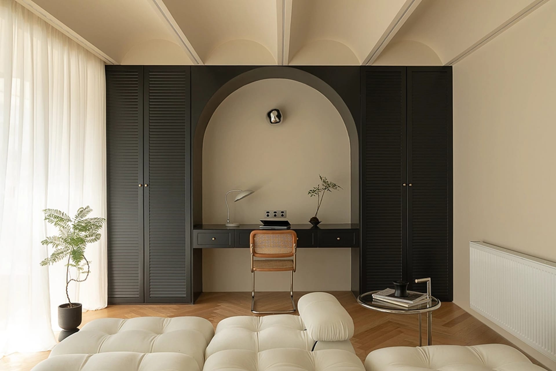 A minimalist home office featuring a sleek black desk with a white cushioned bench and a small potted plant.