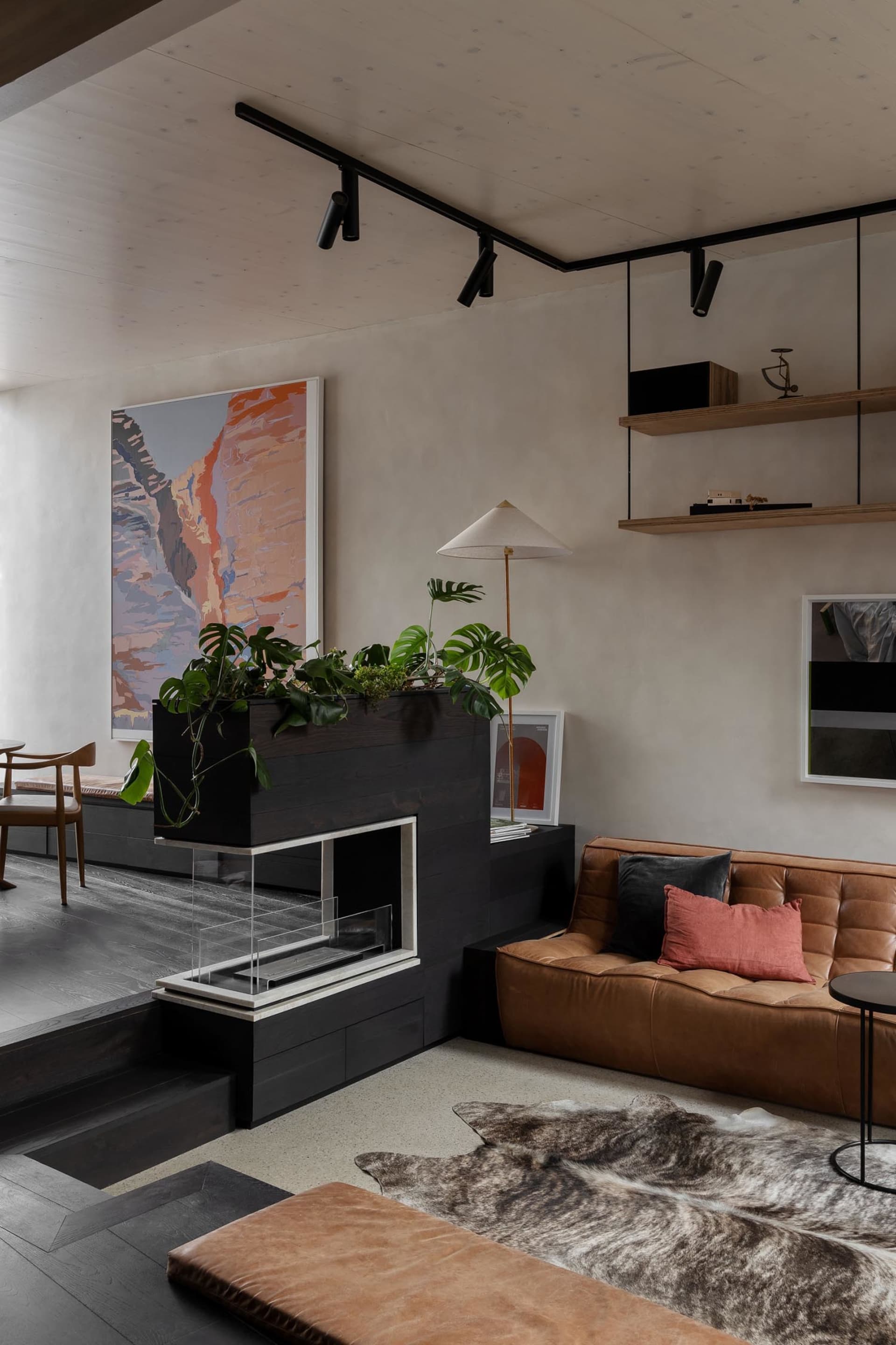 Modern minimalist living room featuring a brown leather sofa, metal floor lamp, wood fireplace, and black and white shelves.