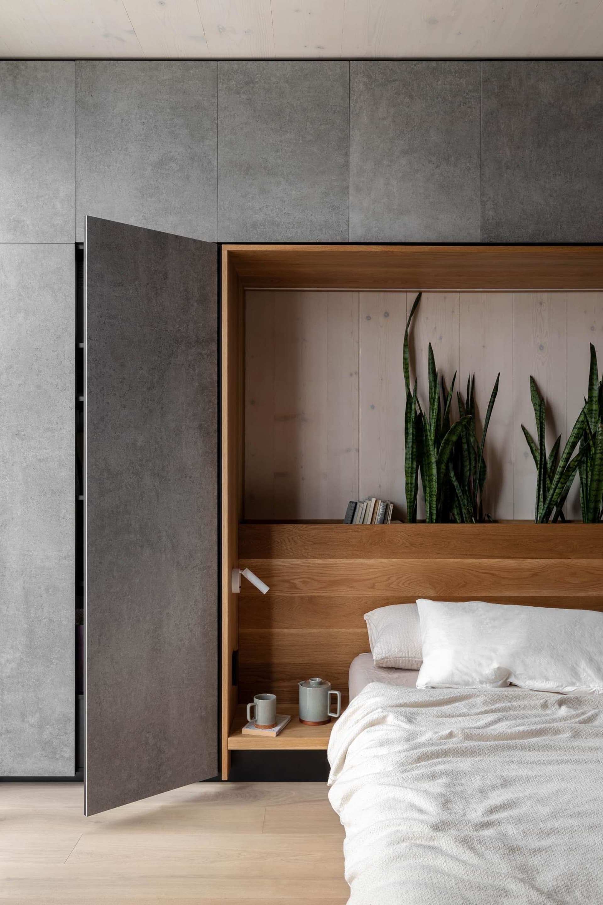 Modern minimalist bedroom featuring a wooden bedframe and a concrete wall with built-in shelves