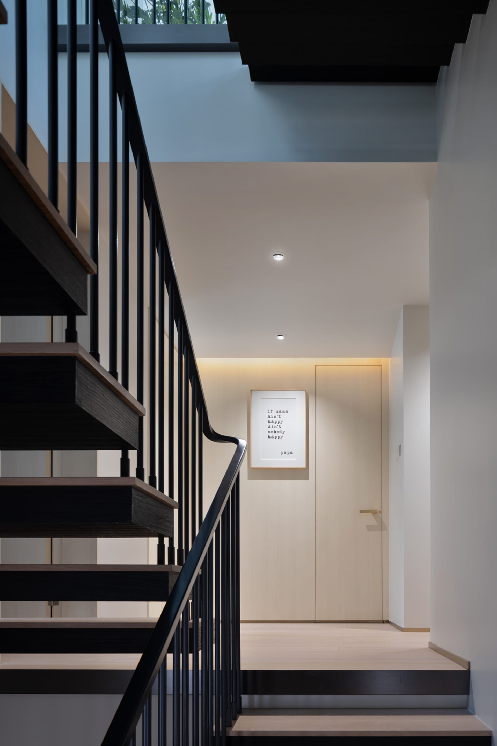 Modern staircase with black handrail and wooden steps against a white wall.