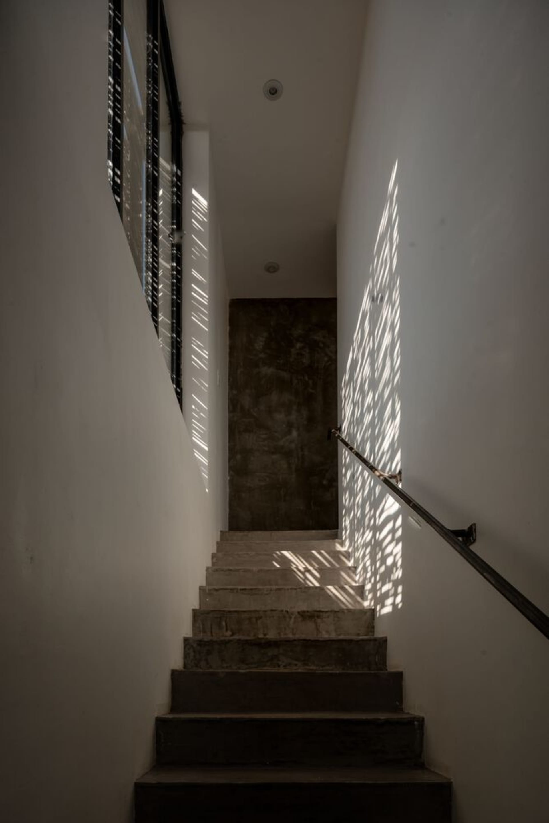 Minimalist staircase with concrete steps, glass barrier, and shadows on the wall.