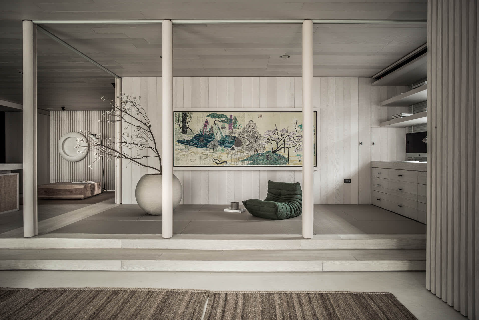 Minimalist living room featuring a wooden floor and furniture, with a large tapestry and a green beanbag chair.