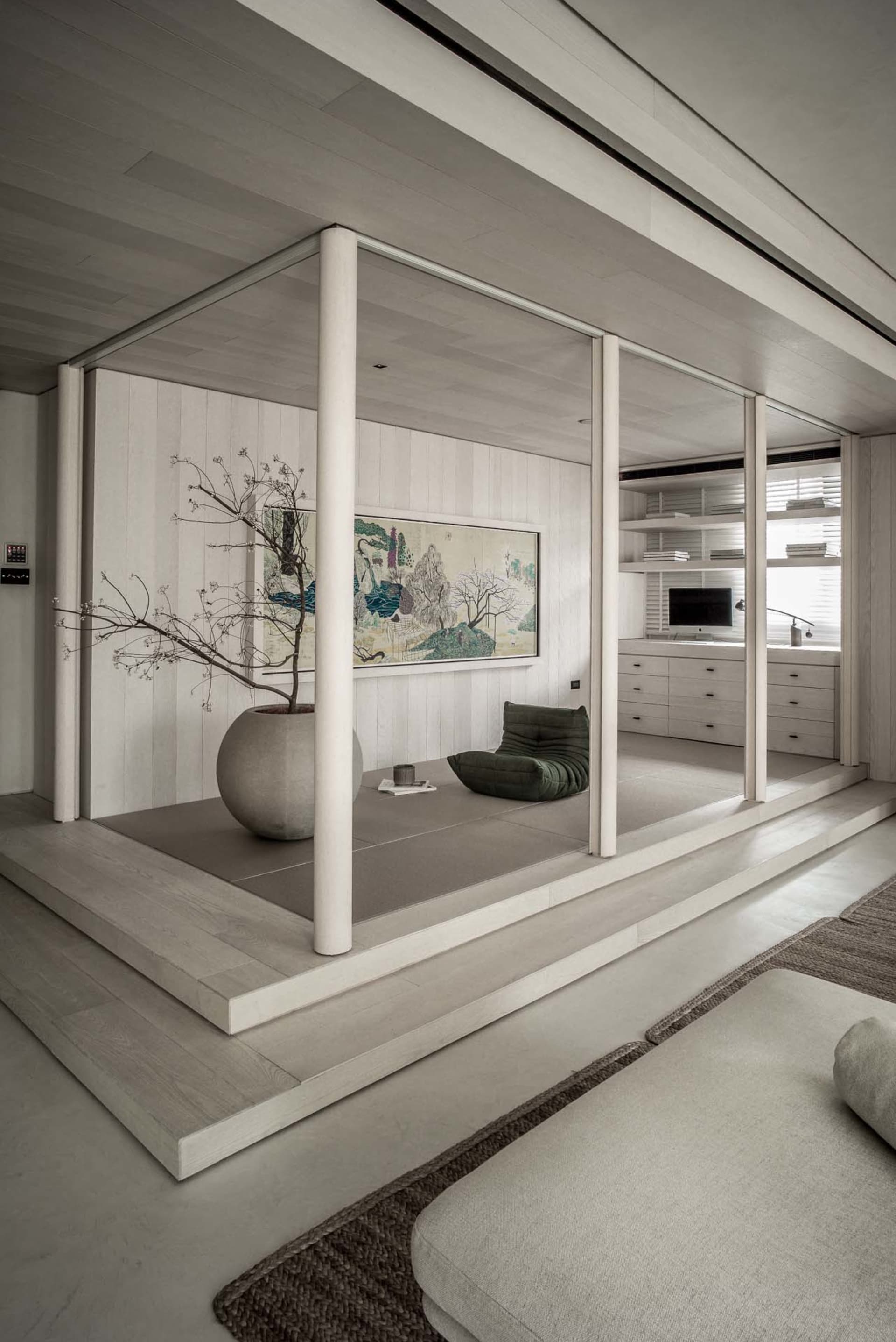 A modern minimalist living room with a Zen pod featuring a potted tree and a framed painting.