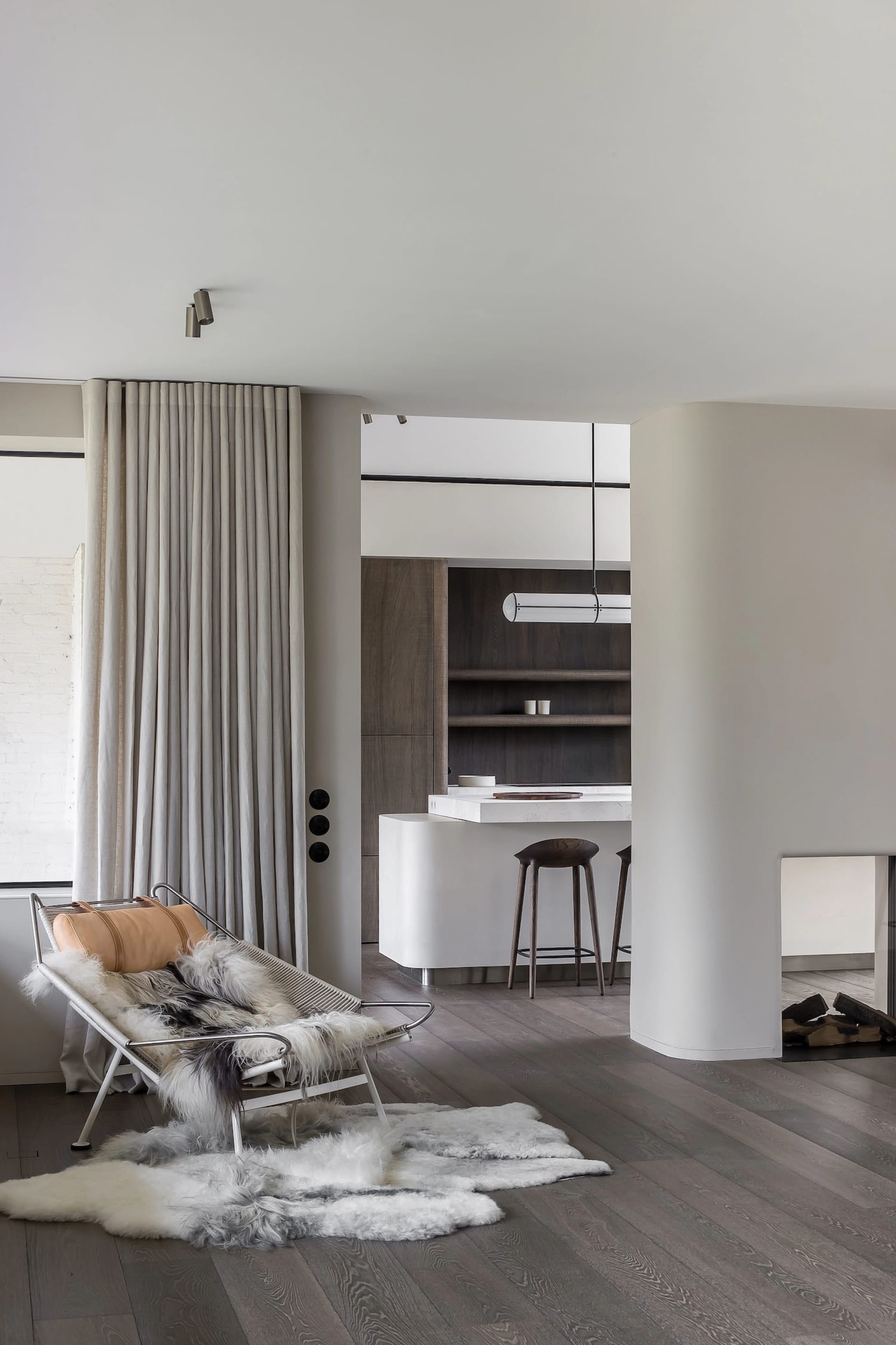 A modern minimalist kitchen with white marble countertops, wooden flooring, and a comfortable lounge area.