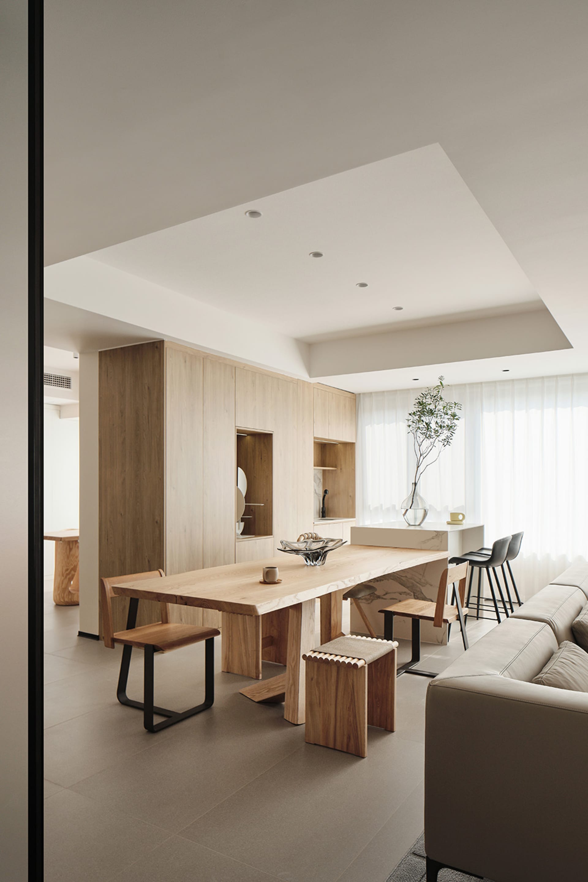 A minimalist living and dining room featuring wood furnishings and soft lighting.