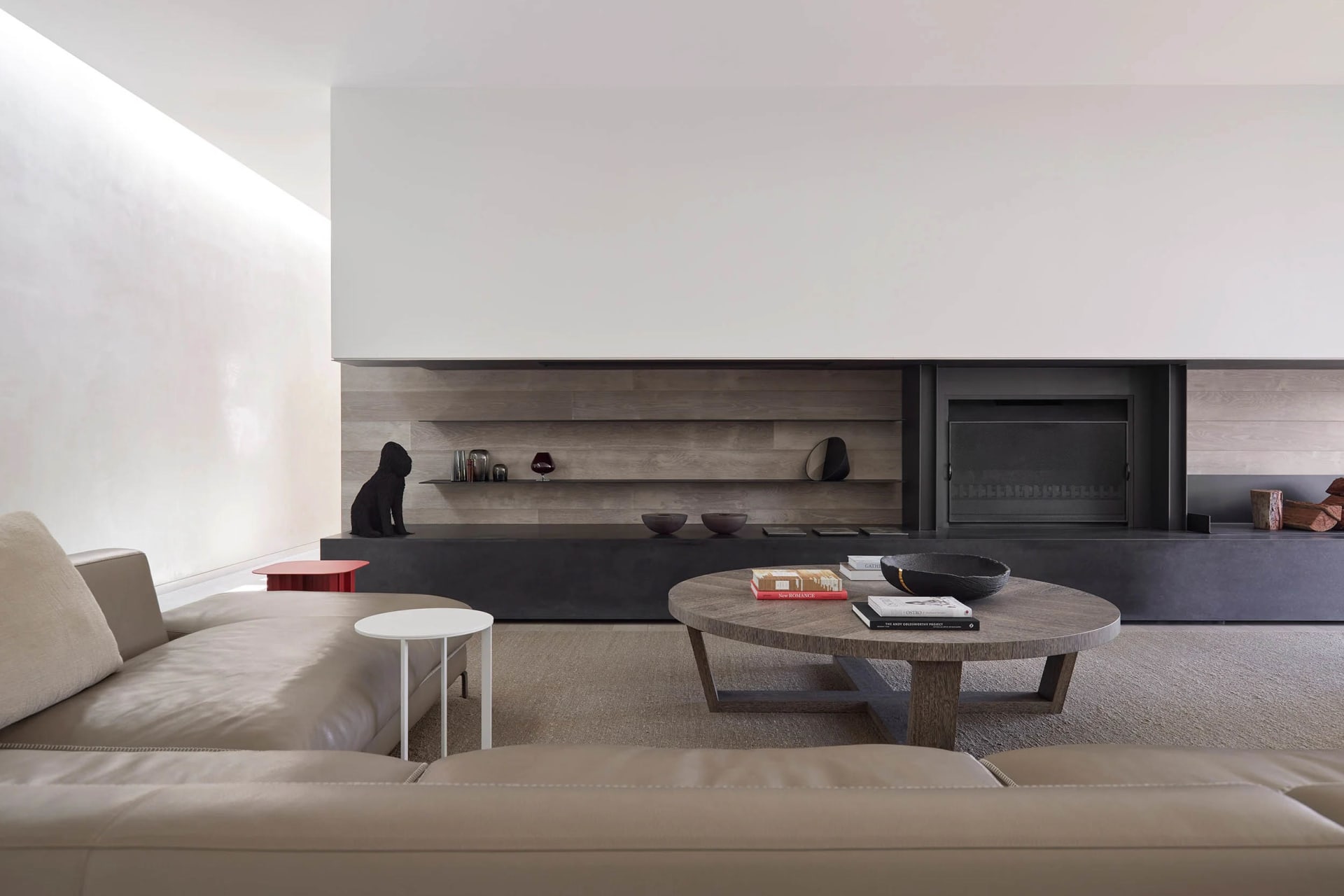 The minimalist living room features a concrete fireplace and wooden coffee table in front of a concrete and wood wall.