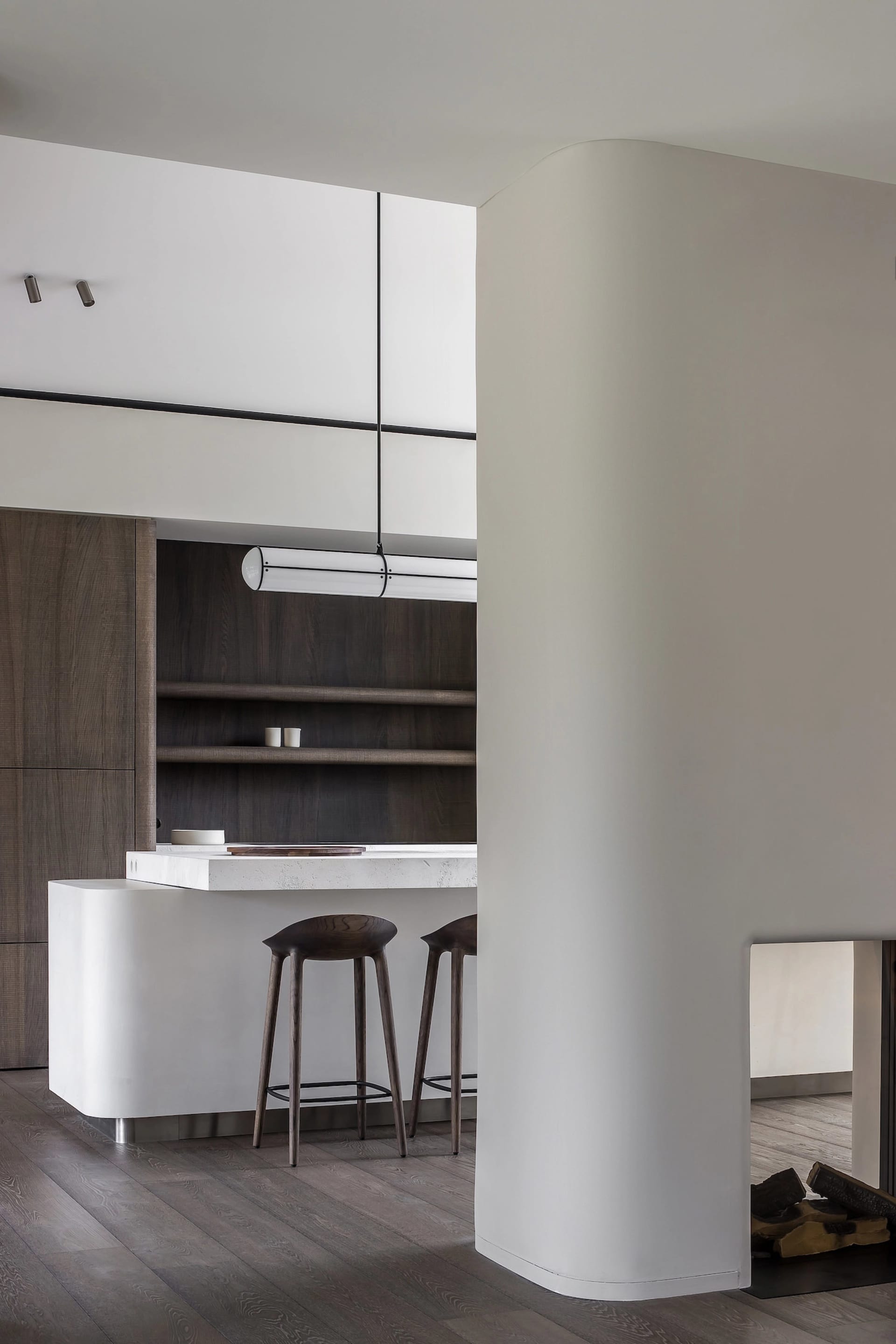 Modern kitchen bar with minimalist design, featuring a white countertop and dark wood stools.