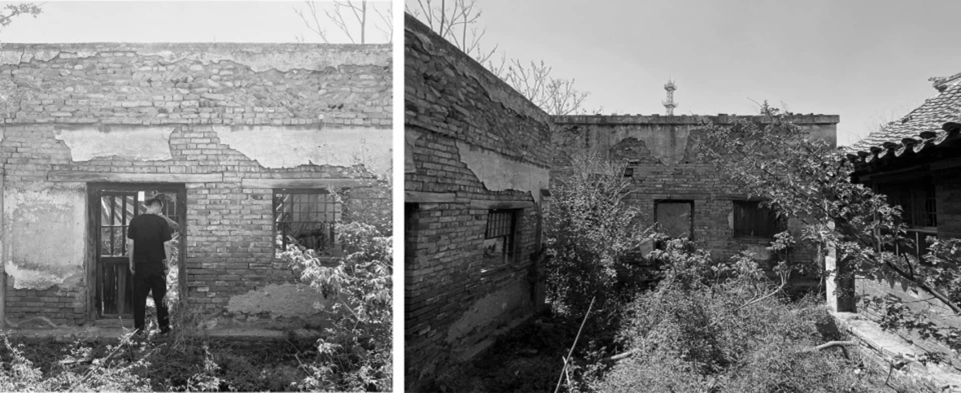 A black and white image showing the ruins of a brick building with damaged walls and overgrown vegetation.