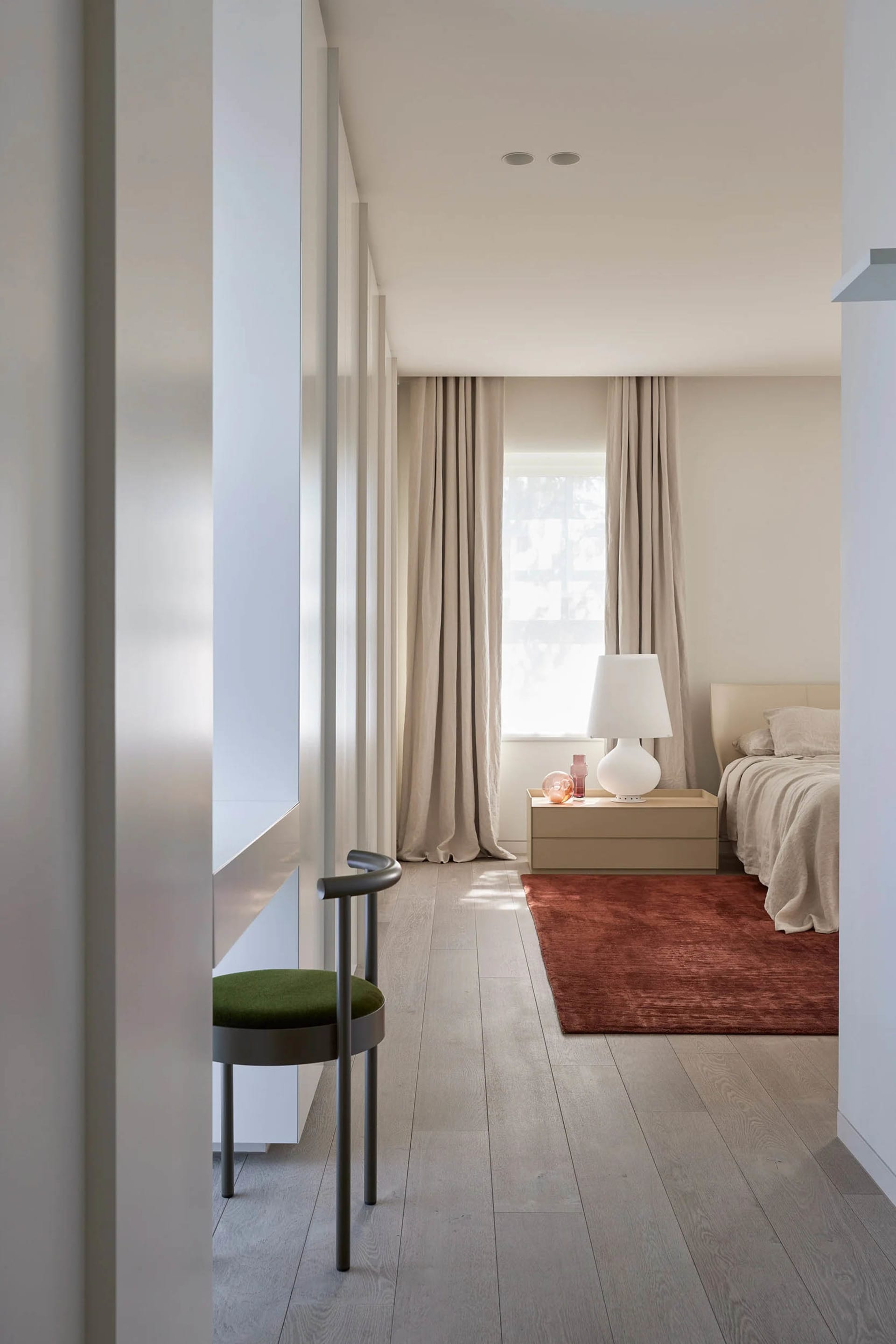 A minimalist bedroom with wooden flooring, a bed, a side table with a lamp, and a green chair against the wall.