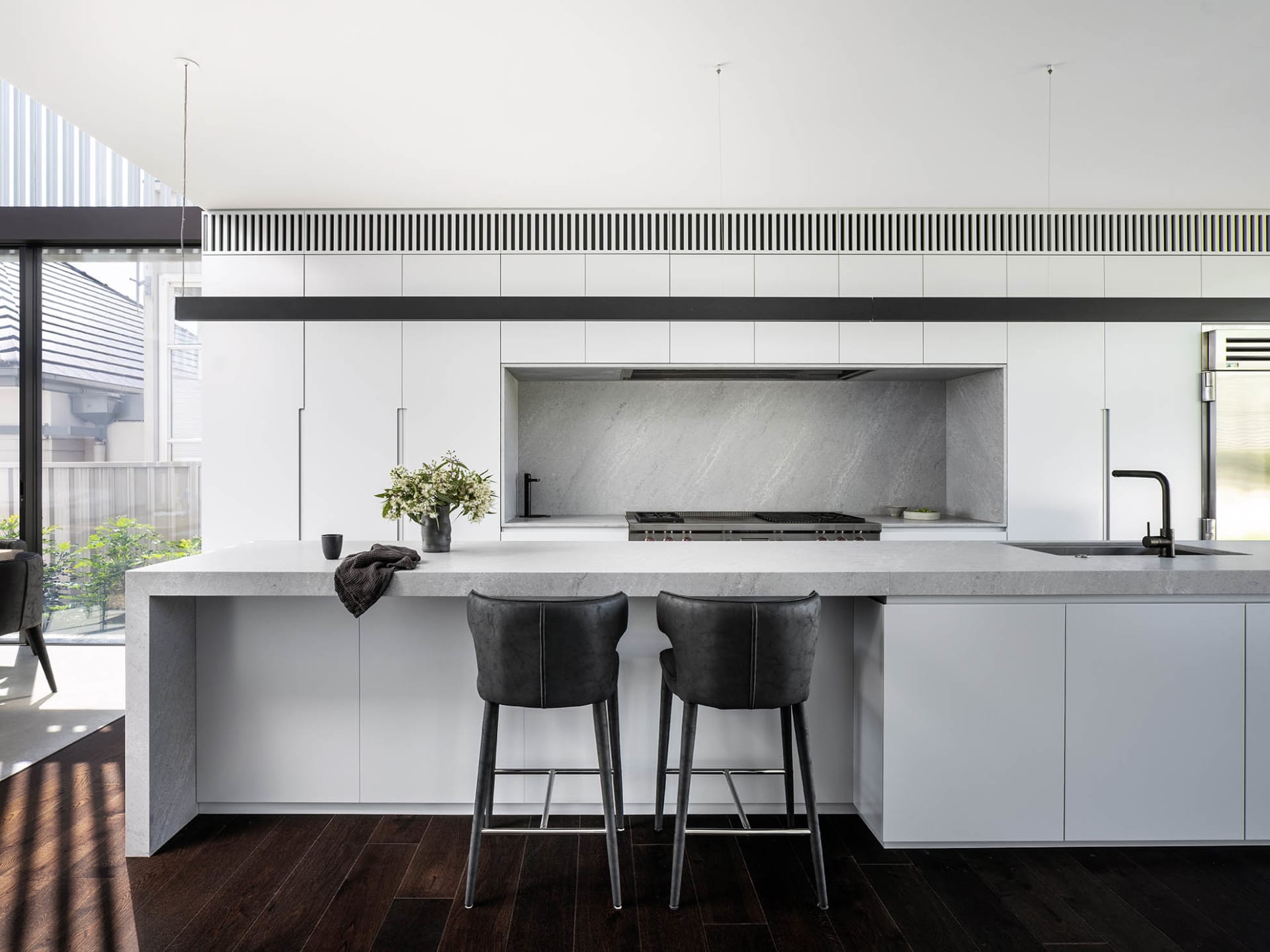 A minimalist kitchen with a concrete countertop, white cabinets, and dark wood flooring.