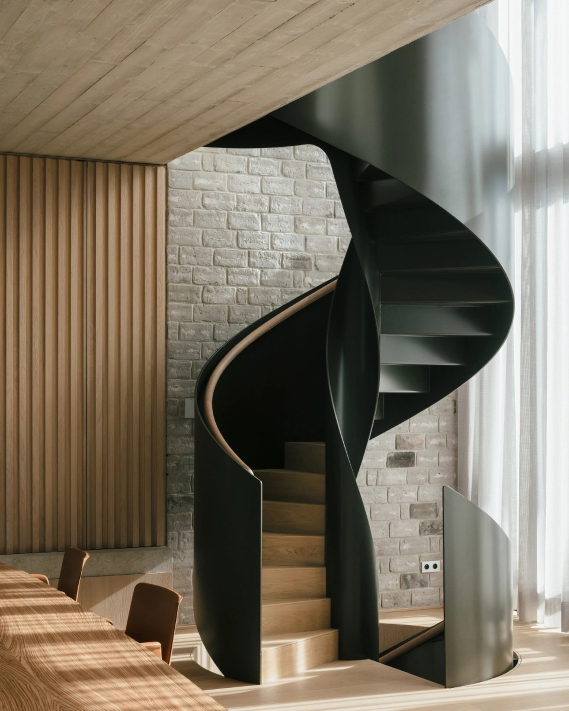 A modern, black metal spiral staircase with wooden steps and railings.