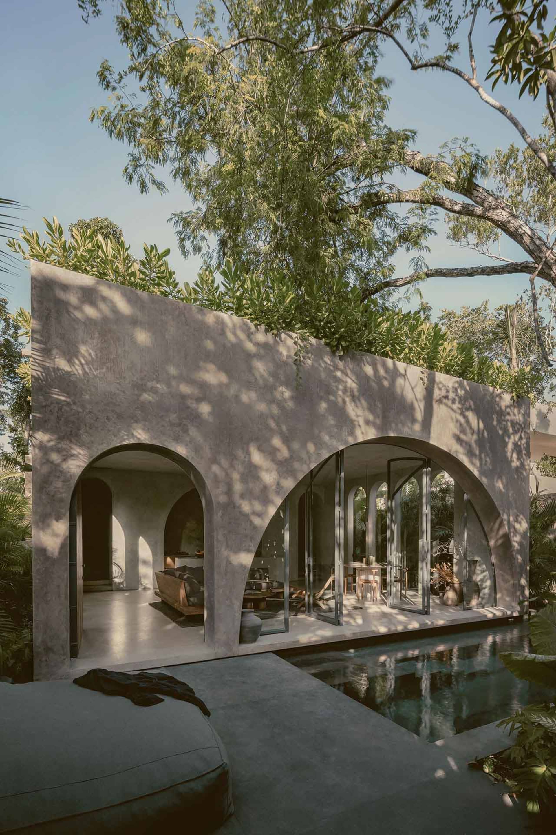 An outdoor living space with a modern design, featuring concrete walls, glass doors, and a pool.