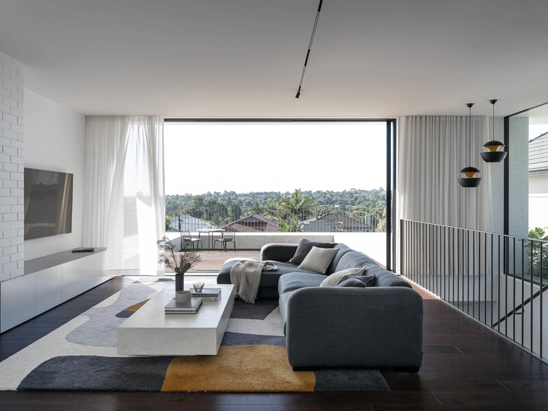 A modern living room with a grey sofa, concrete floors, and large windows.