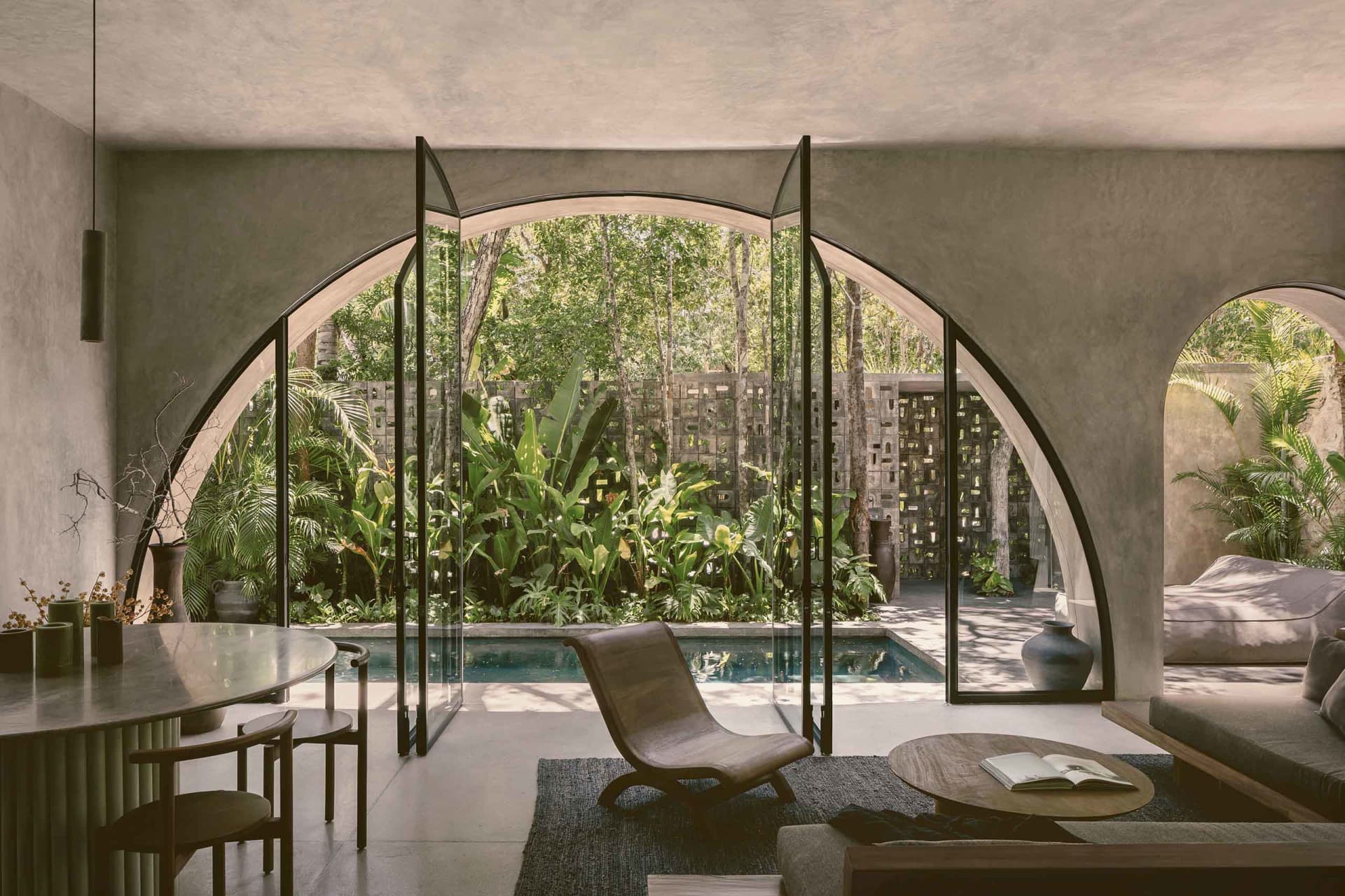 Modern residential interior featuring concrete walls and glass doors with a view of a pool and garden.