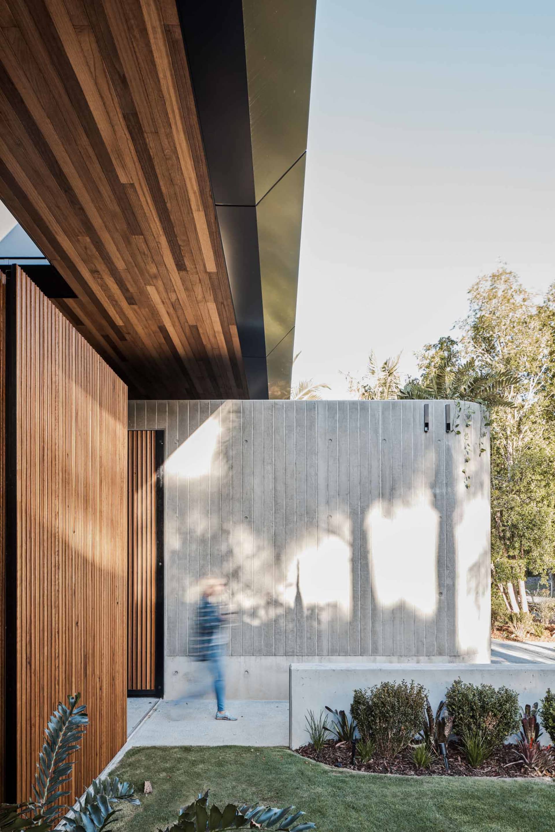 A modern residential entryway featuring a wooden door and a concrete wall with a large, illuminated window.