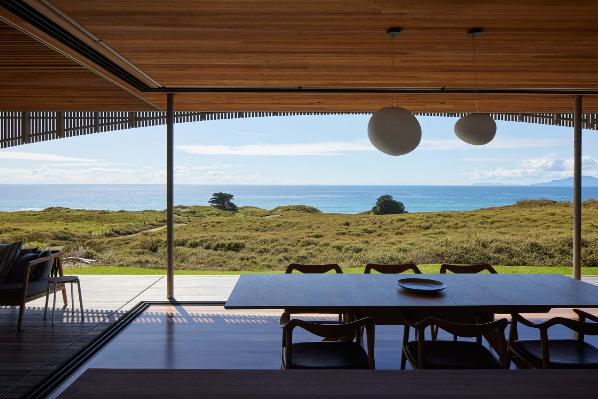Modern residential interior featuring wood, glass, and metal materials with a sea view.