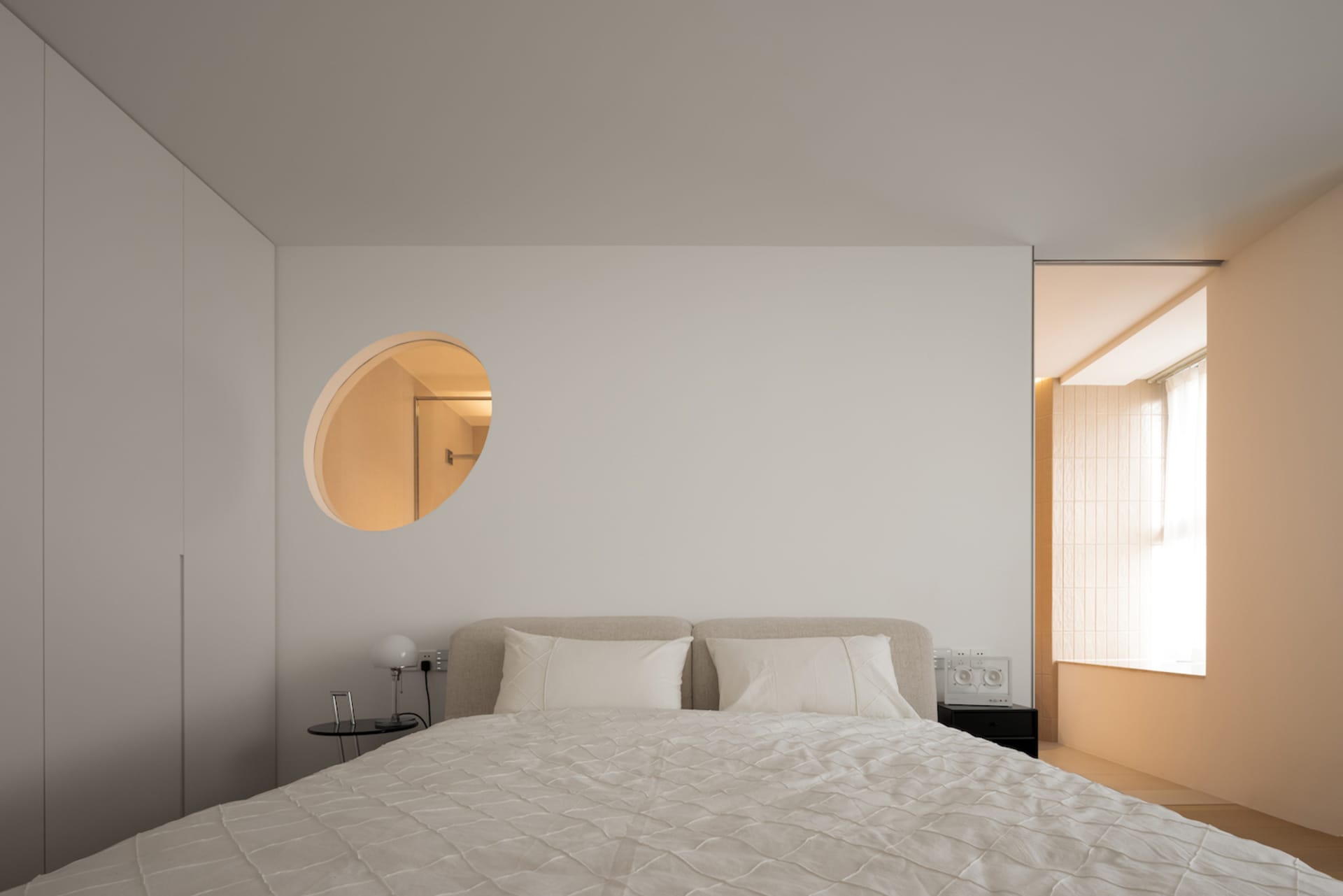 A minimalist bedroom with a fabric-covered bed and light wood accents