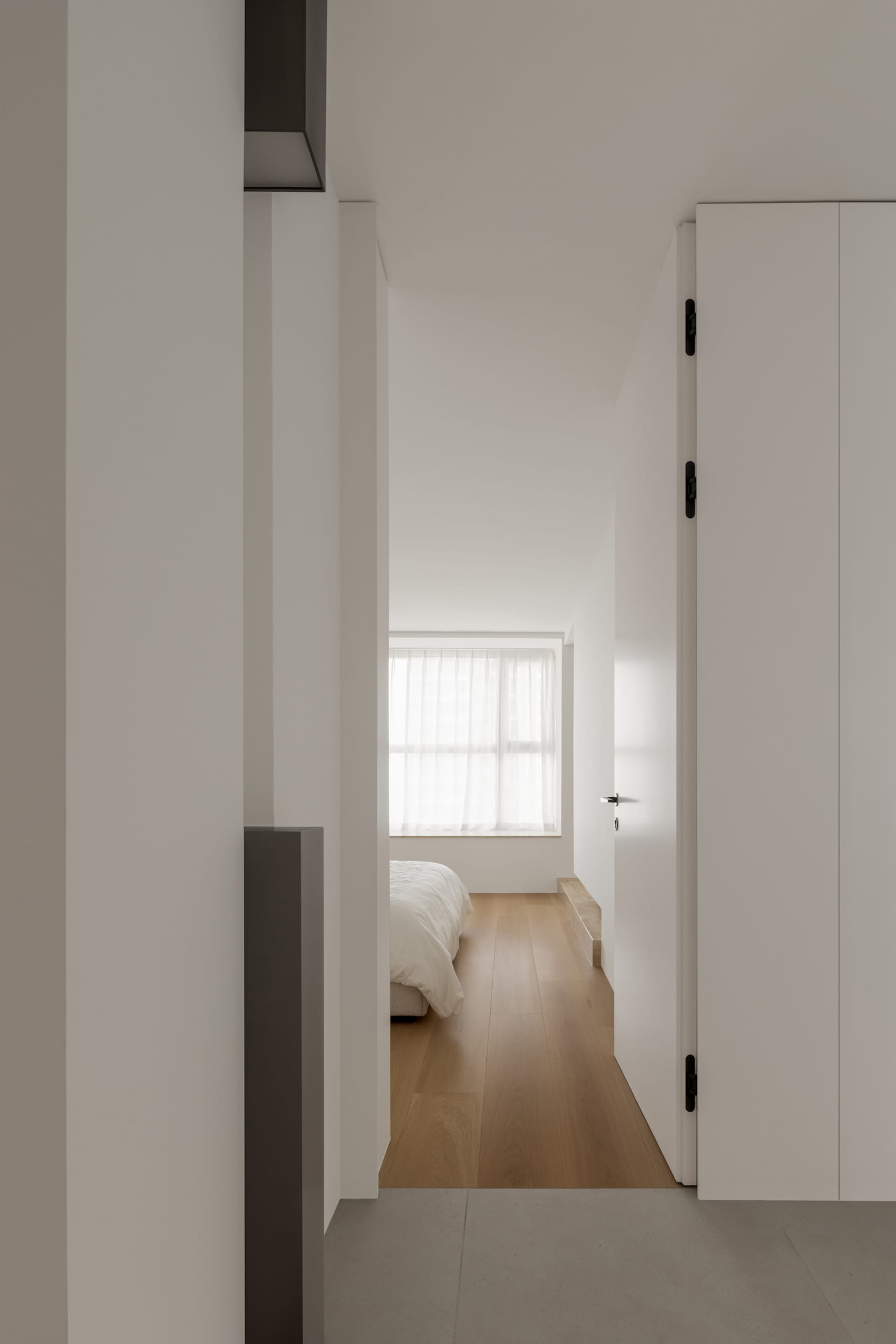 A minimalist bedroom with wood flooring and a bed.