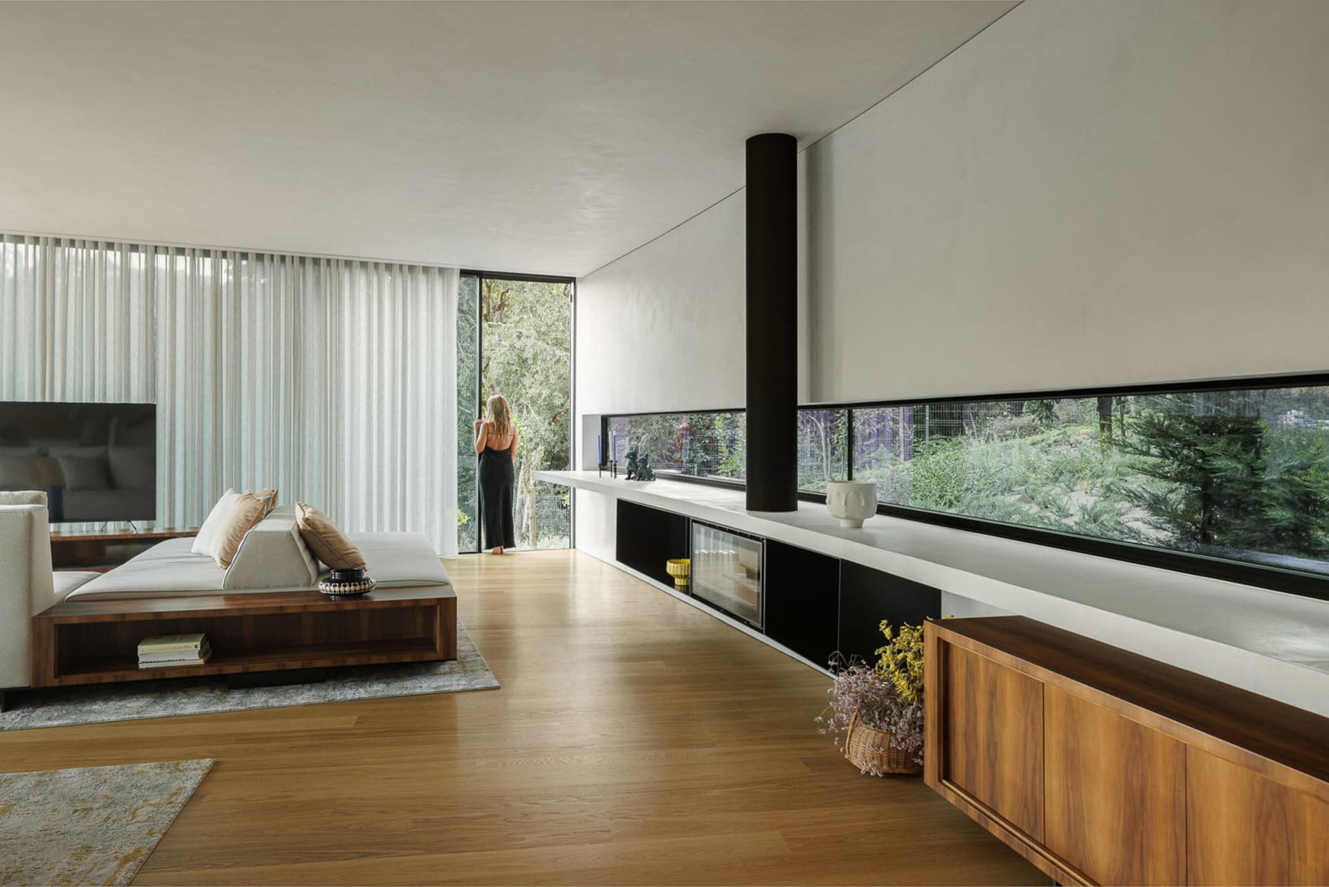 Modern minimalist living room featuring wooden flooring, glass walls, and concrete accents.