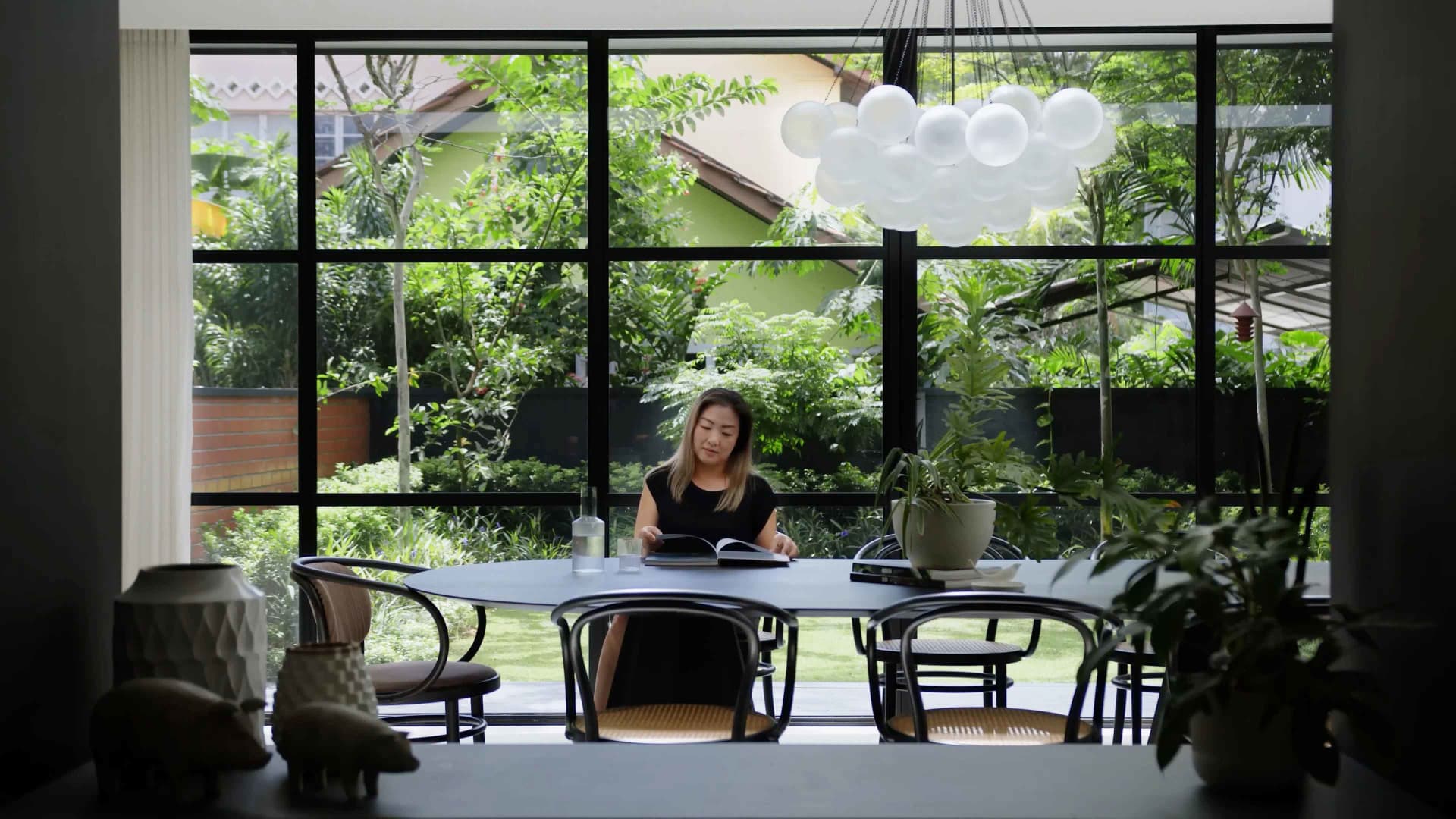 A modern home office featuring a round dining table with metal and glass chairs surrounded by plants, set against a backdrop
