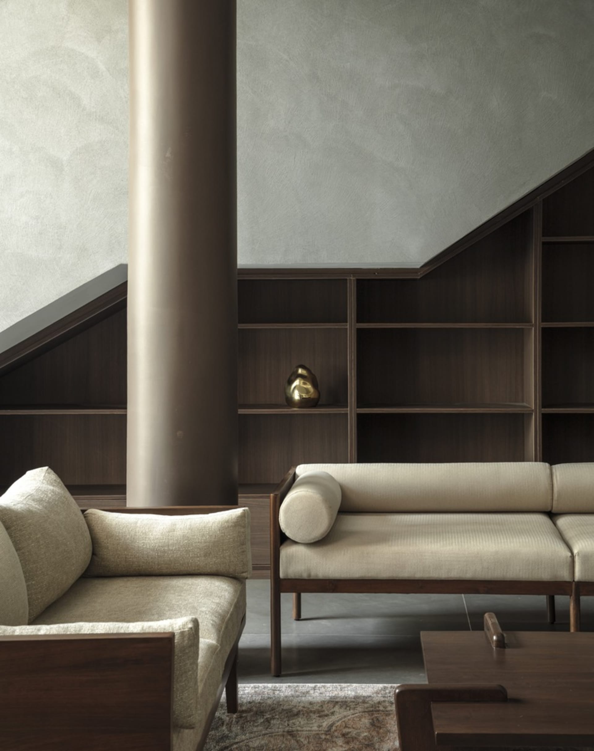 A modern living room with a textured wooden column, upholstered fabric seating, and dark wood shelves against a textured wall