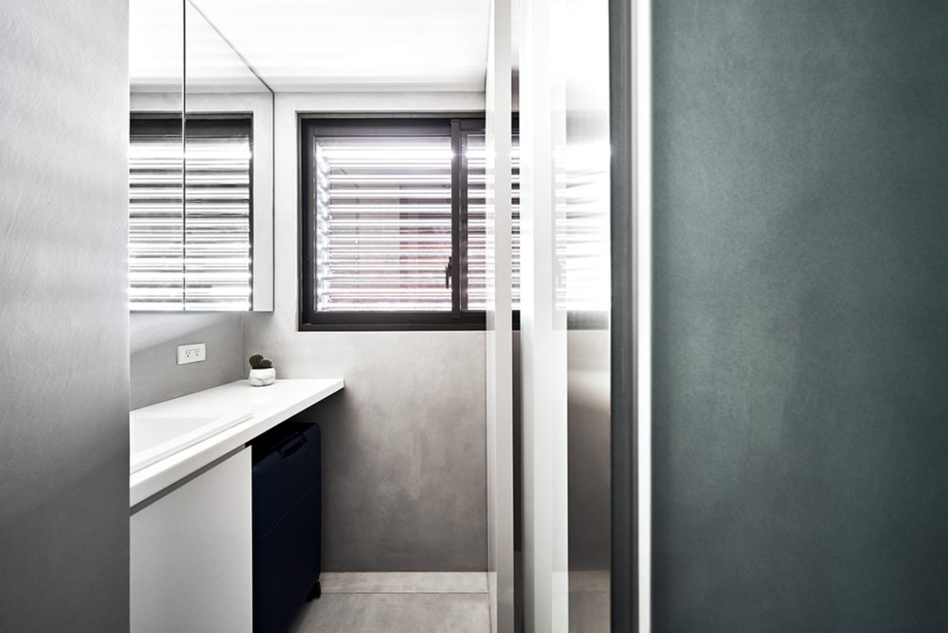 A minimalist bathroom with concrete walls and floor, featuring window blinds and modern fixtures.