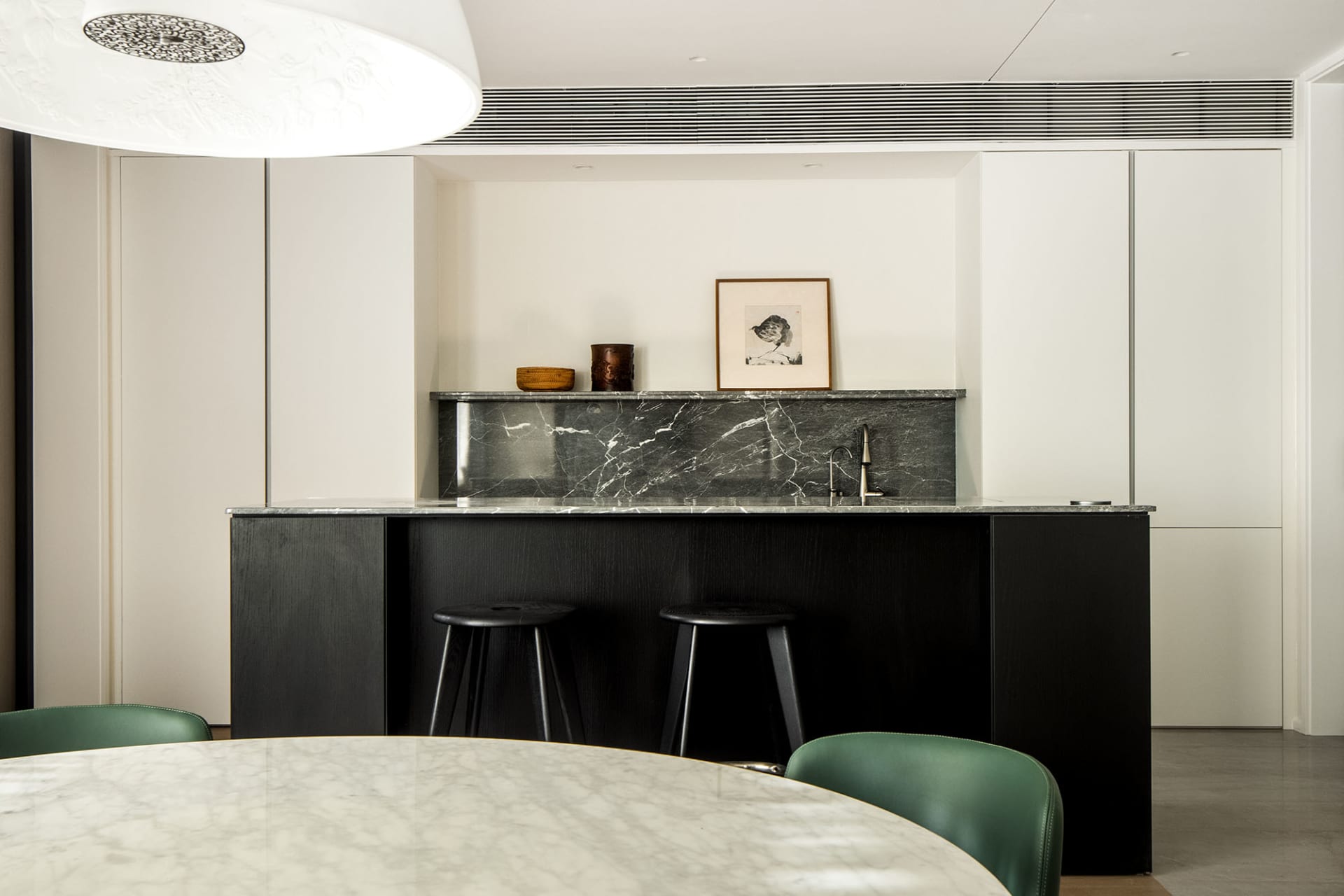 A minimalist kitchen interior with a marble countertop and black bar stools.