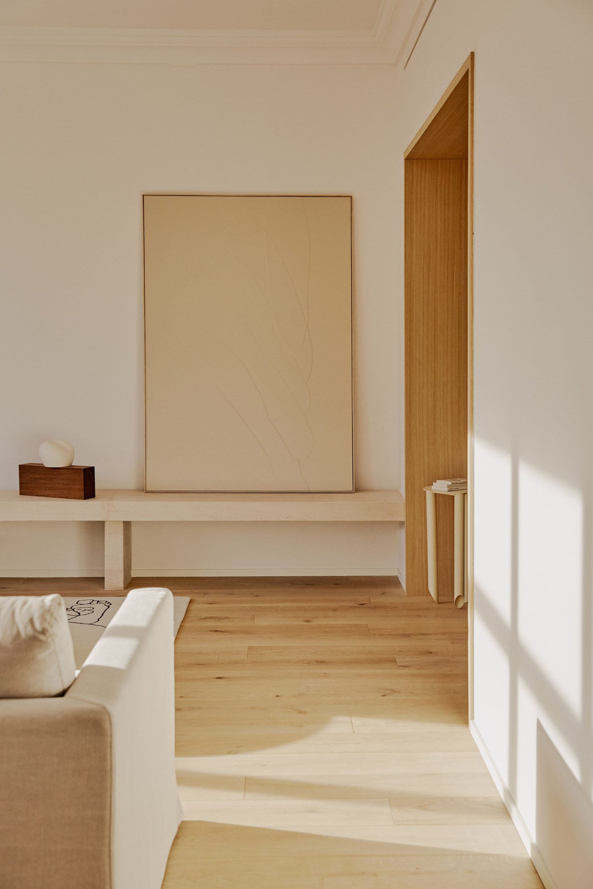 A minimalist living room with natural wood furniture and a large abstract painting.