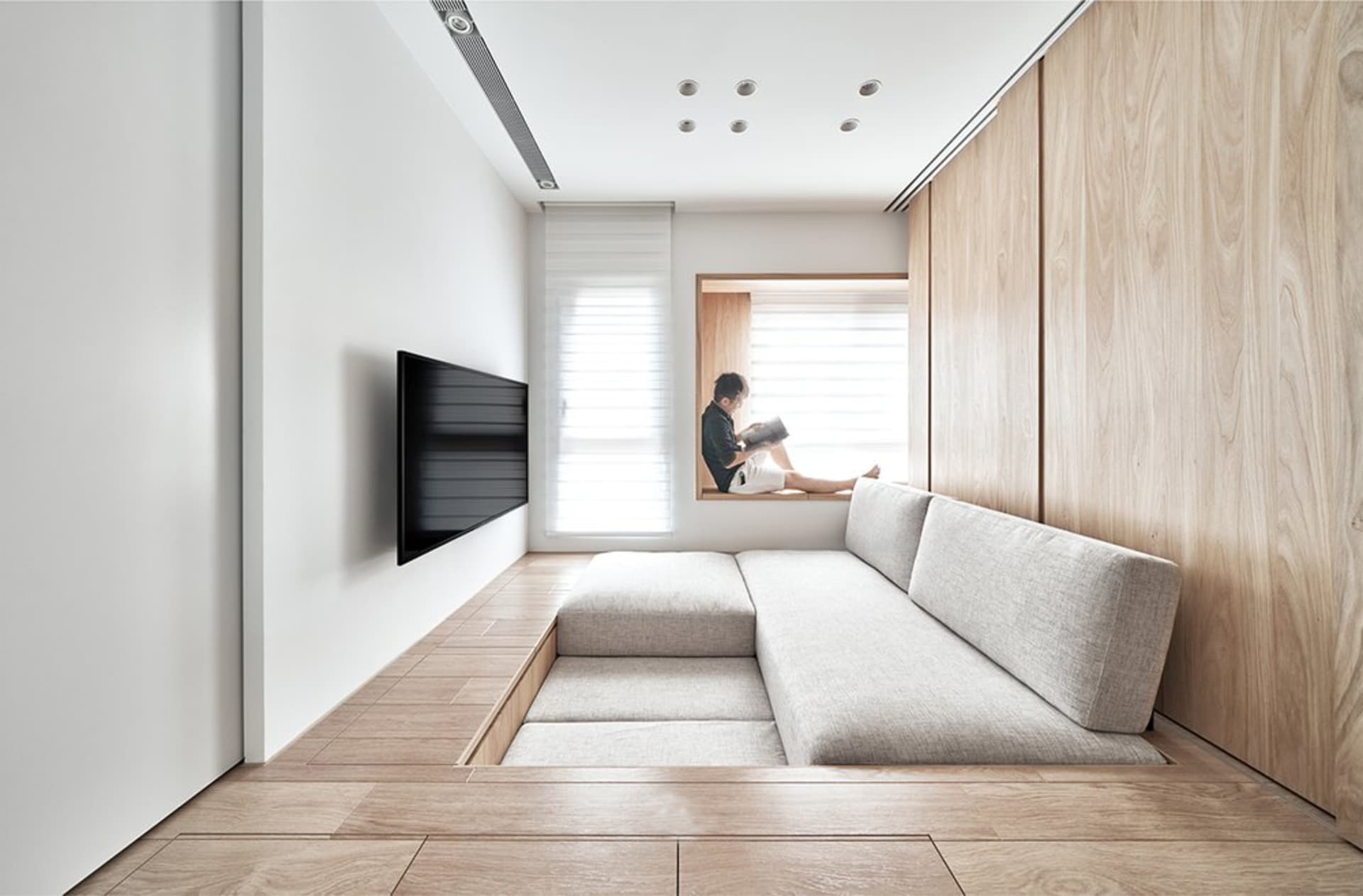 A well-designed minimalist living room with light-colored wooden flooring, a wooden and textile sofa, and a window seat area.