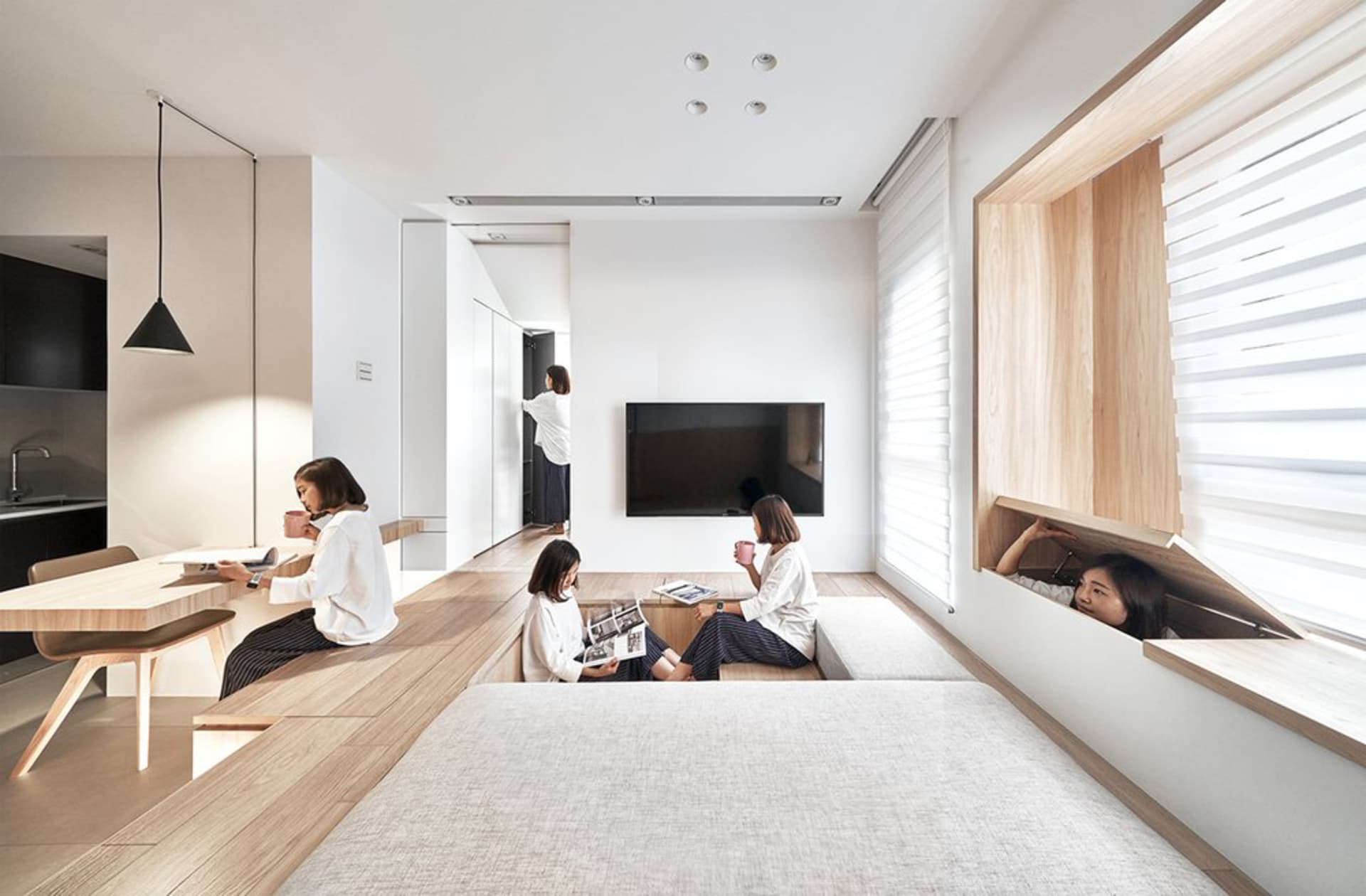 Group of women enjoying coffee in a modern minimalist residential setting with wooden furniture and white walls.