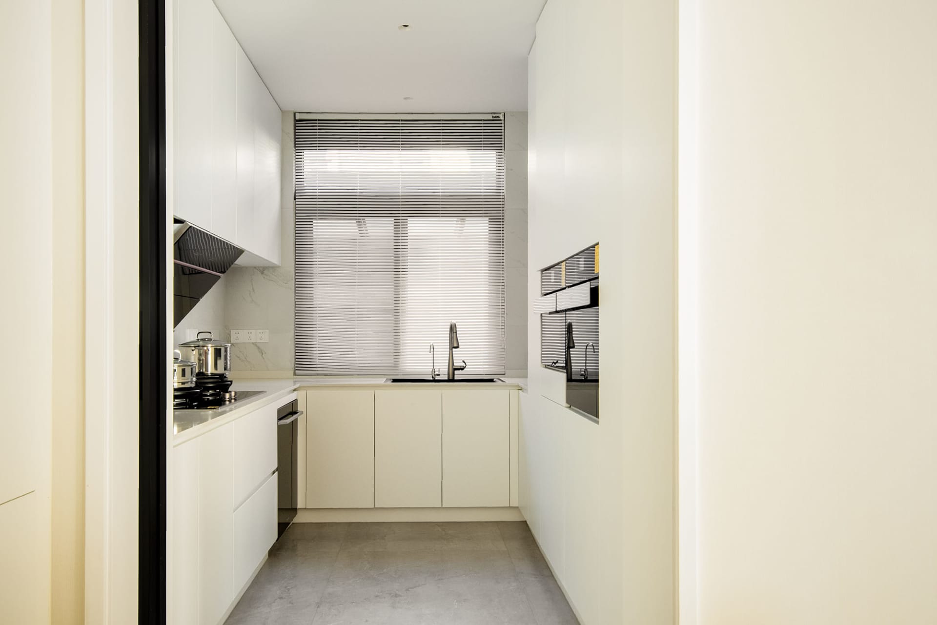 A modern white kitchen with white cabinets, a white countertop, and a large window.