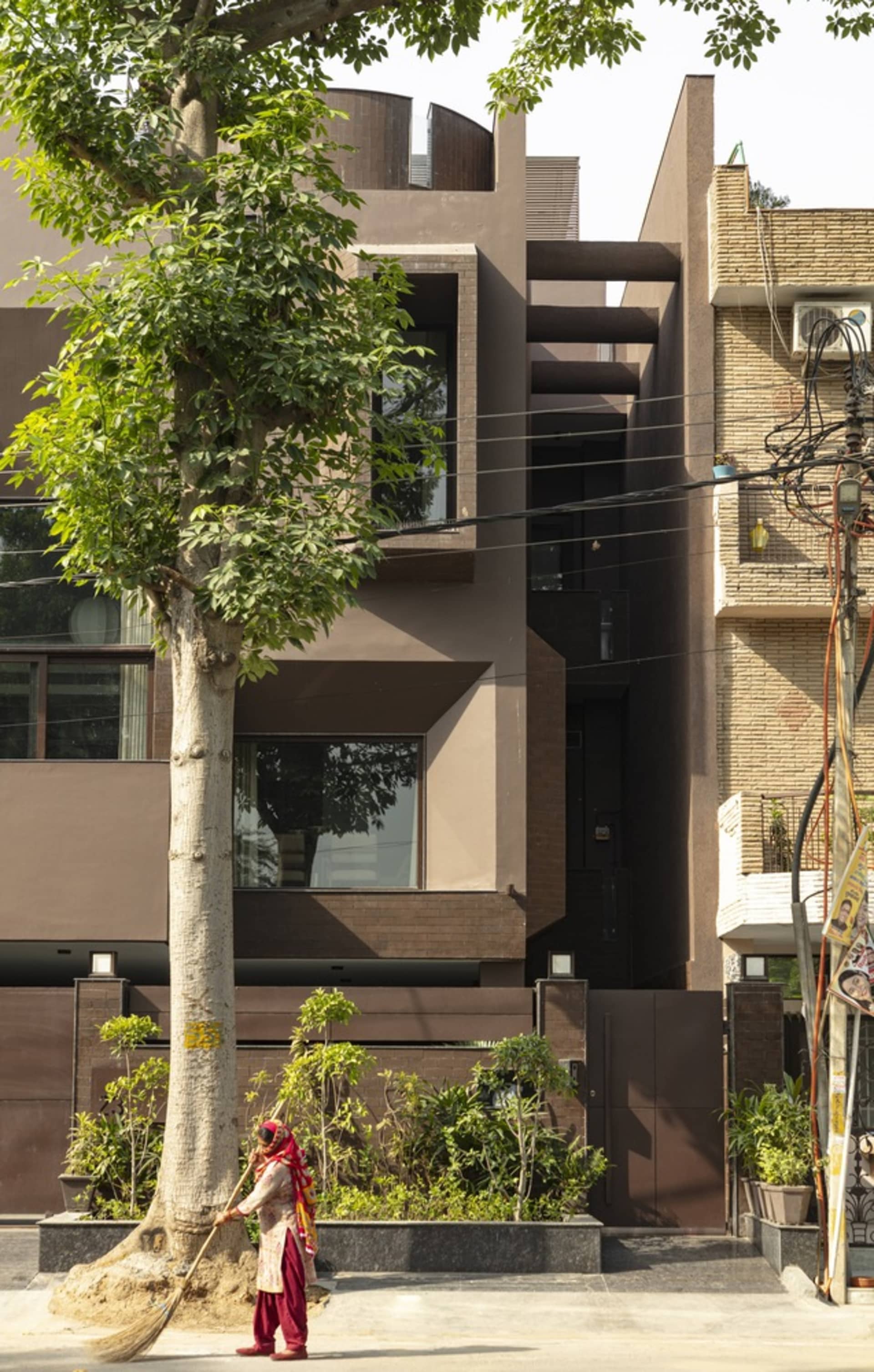 現代住宅建築採用玻璃與磚牆外觀，搭配一棵樹與一位正在清掃人行道的女性。