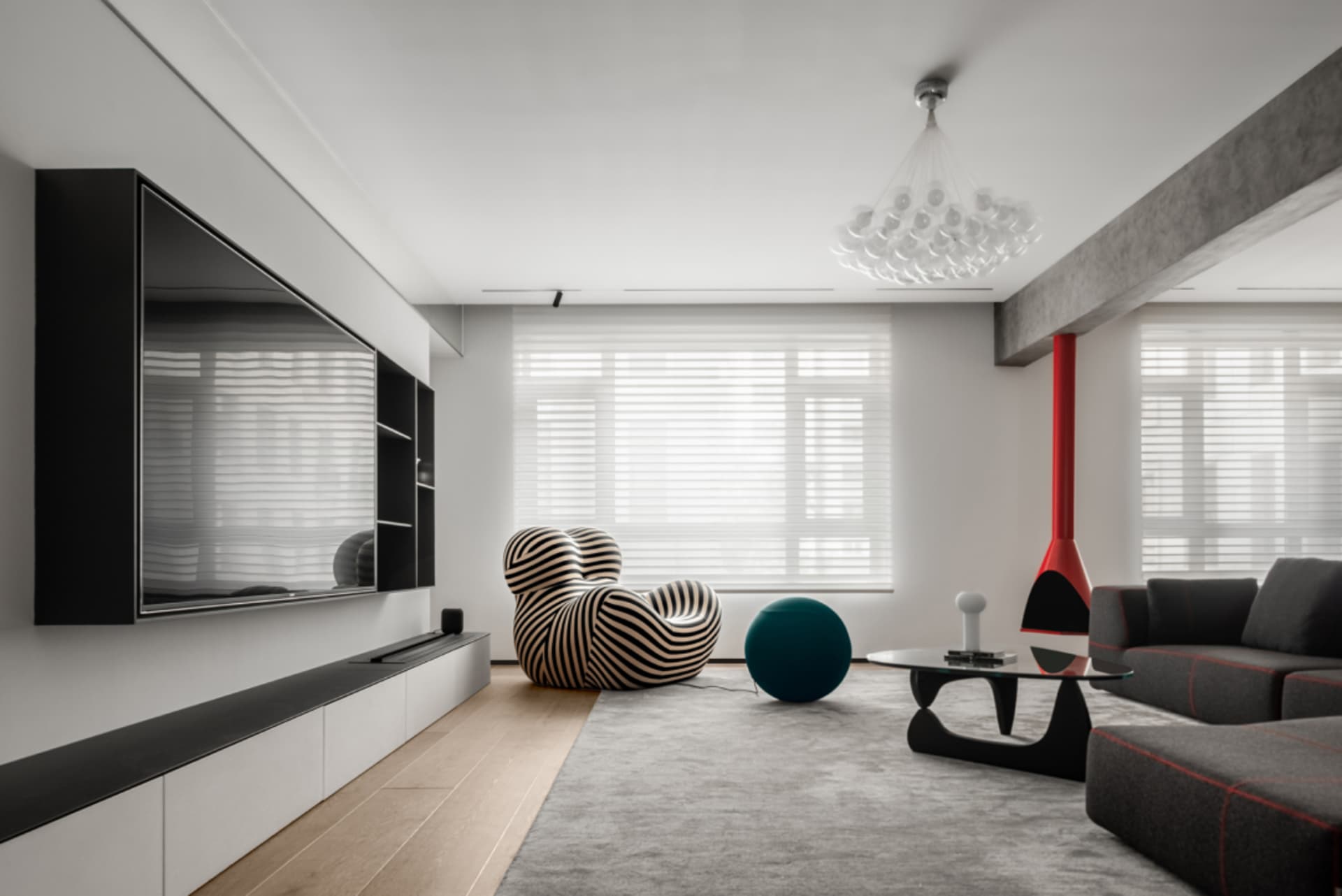 Modern living room with concrete elements, featuring a black and white striped armchair, a teal ball, and a large flat-screen