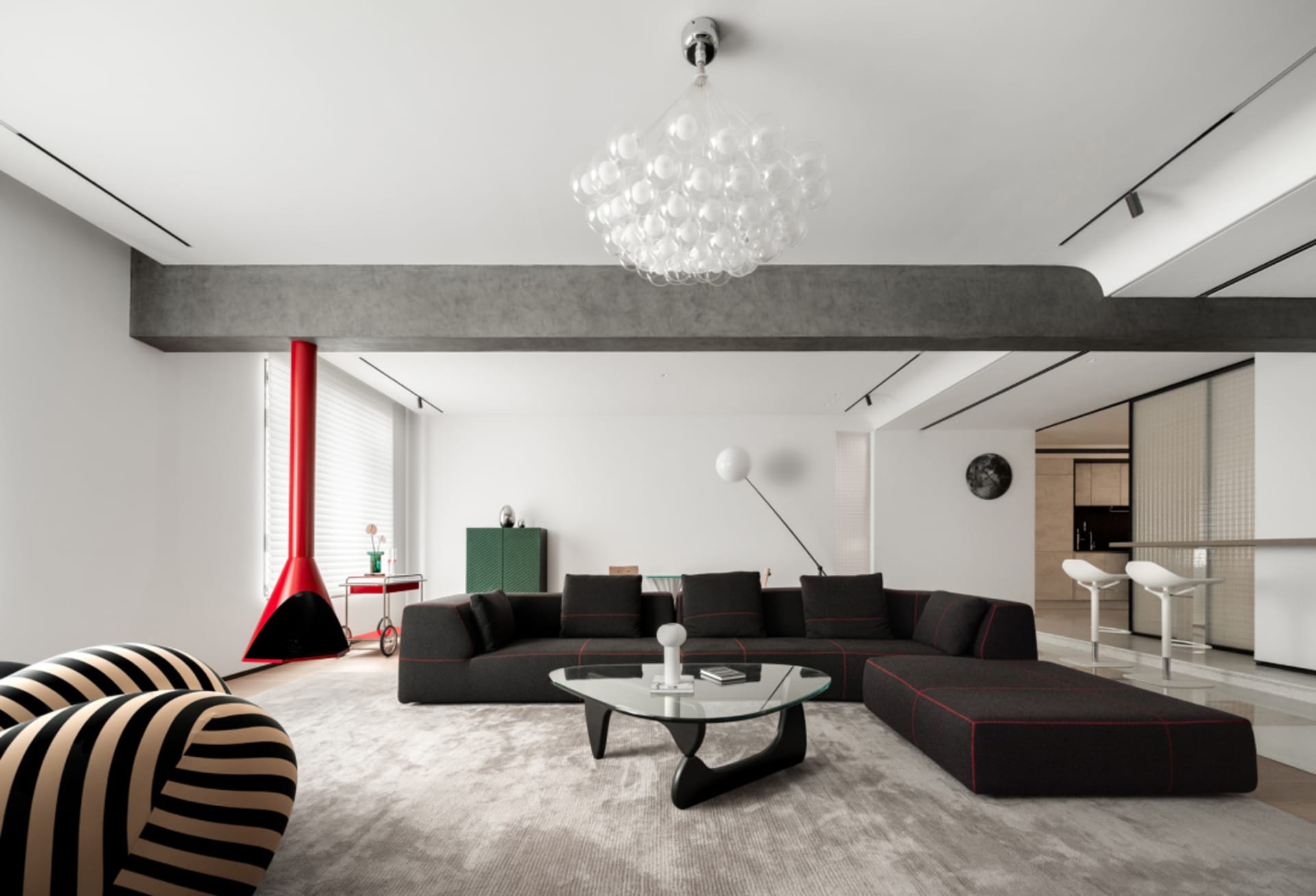 A modern living room featuring a concrete beam, a glass fireplace, and black sofas with red accents on a plush carpet.